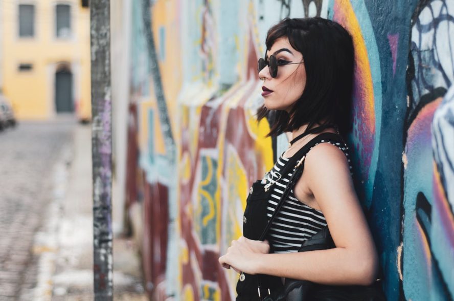 Woman with dark hair and sunglasses wearing a striped shirt against and graffiti wall.