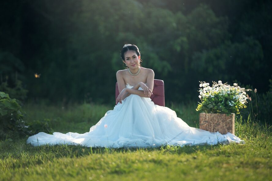 Bride sitting in a white wedding dress in a green field with wildflowers.