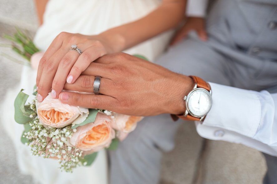 Bride and groom holding hands over a bouquet.