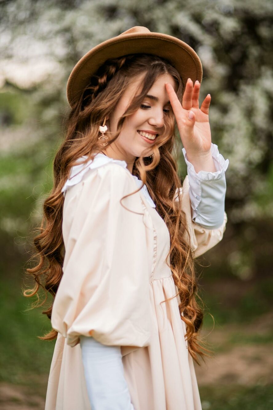 Young woman with long wavy brown hair wearing a hat.