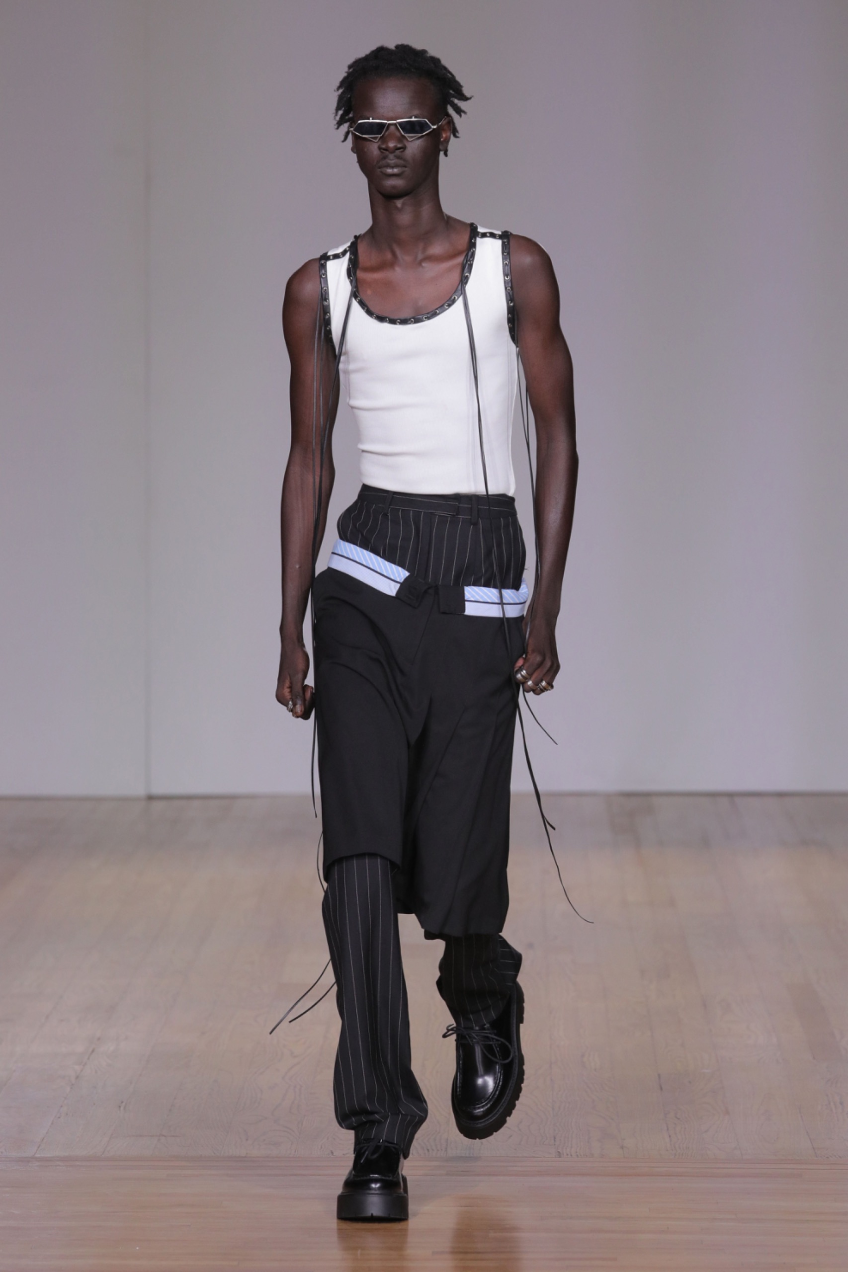 A model walking the runway wearing white vest and black pants.