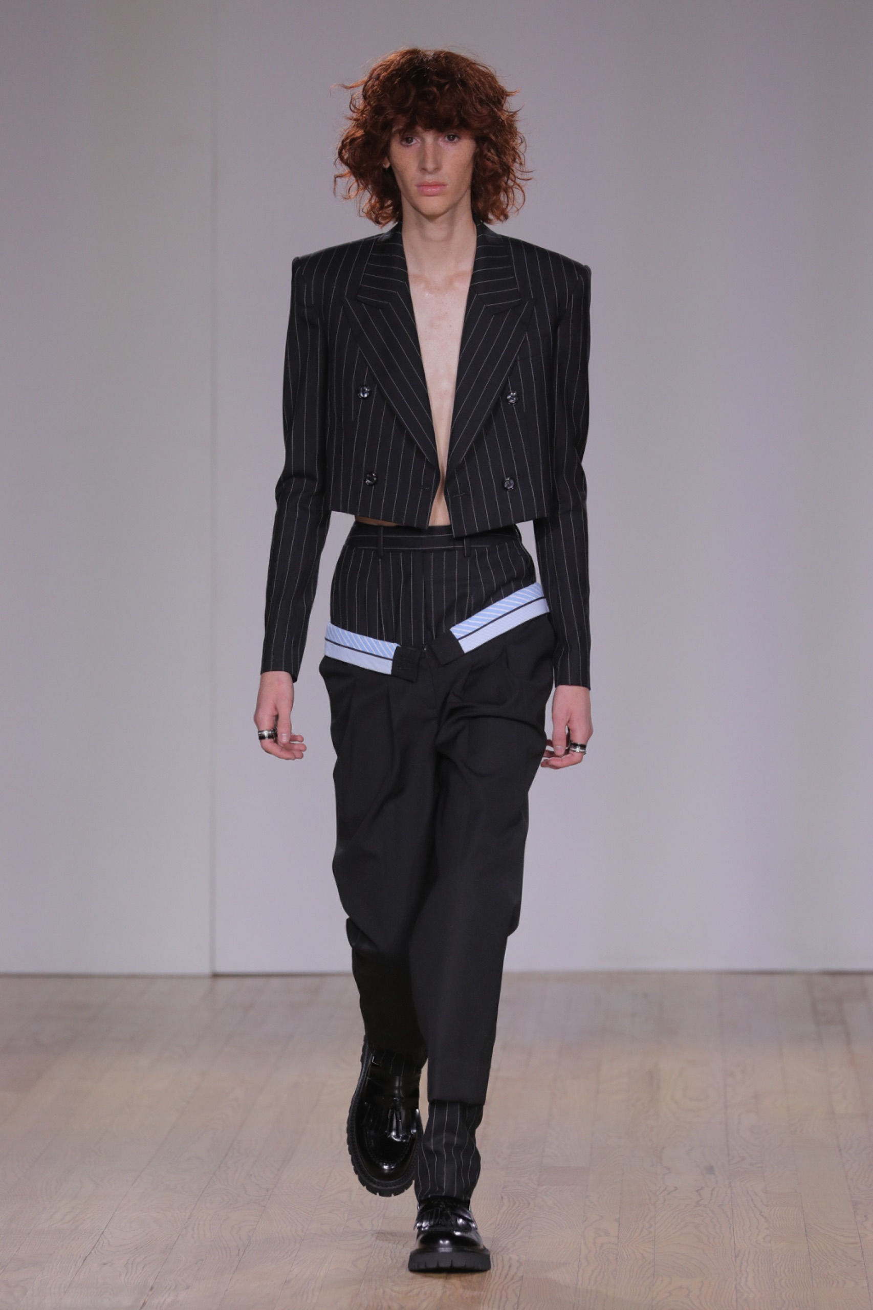 A model walking the runway wearing a black blazer and black pants.