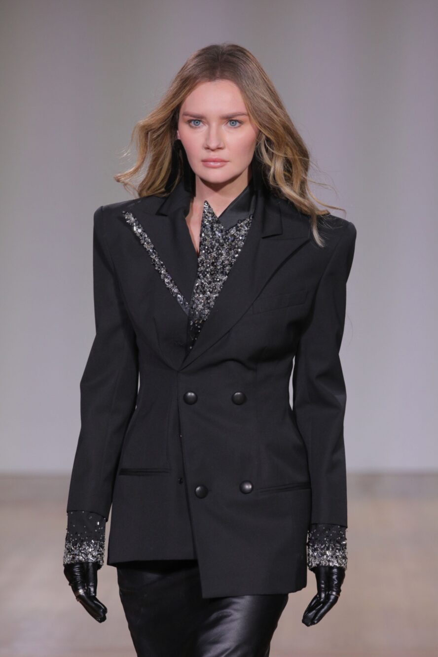 A model walking the runway wearing black gloves, jacket and skirt.