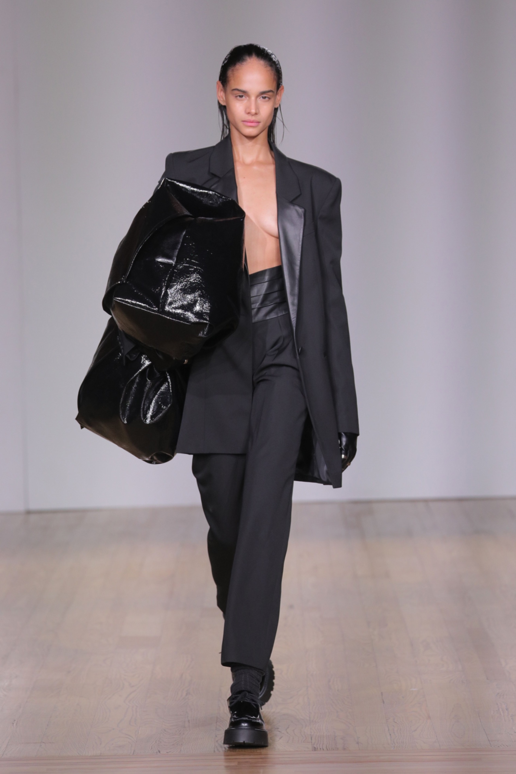 A model walking the runway wearing black blazer, black pants and black bag.