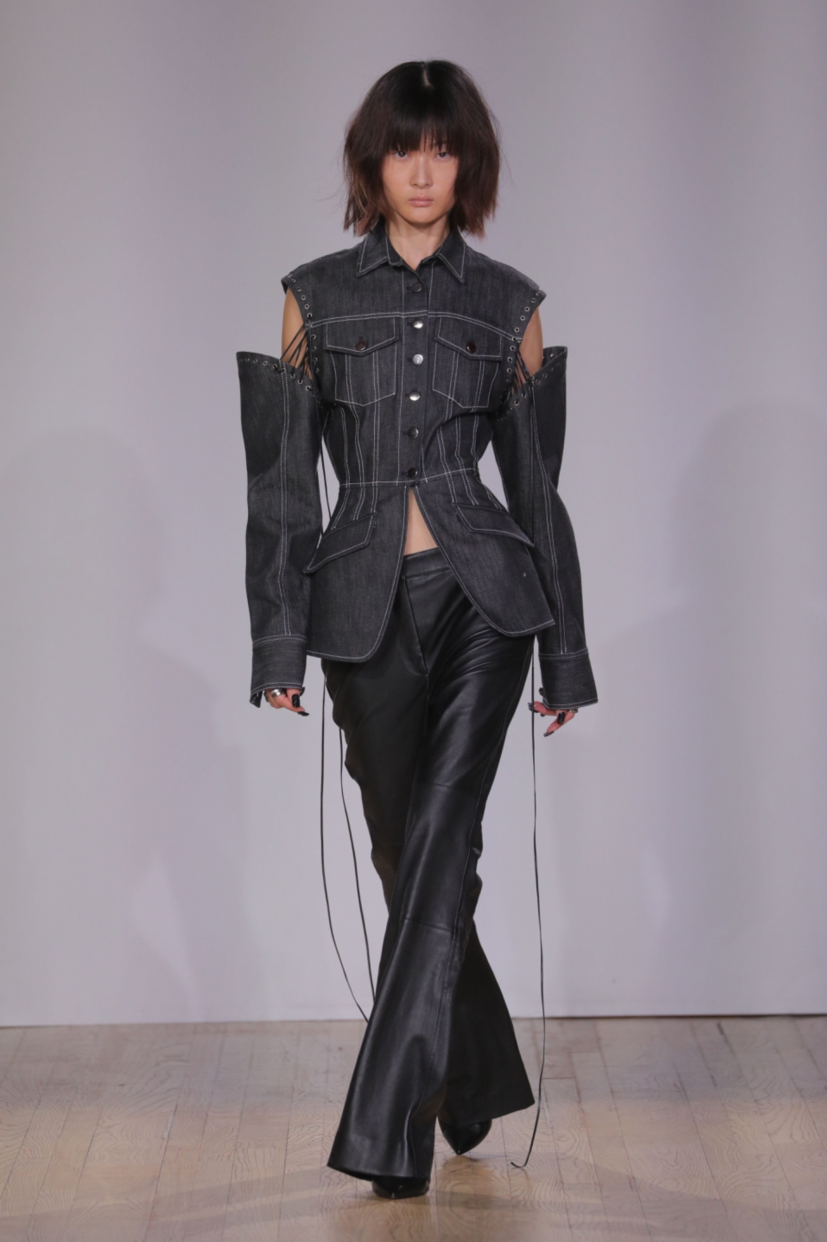 A model walking the runway wearing a dark grey vest, long unattached sleeves and bottoms.