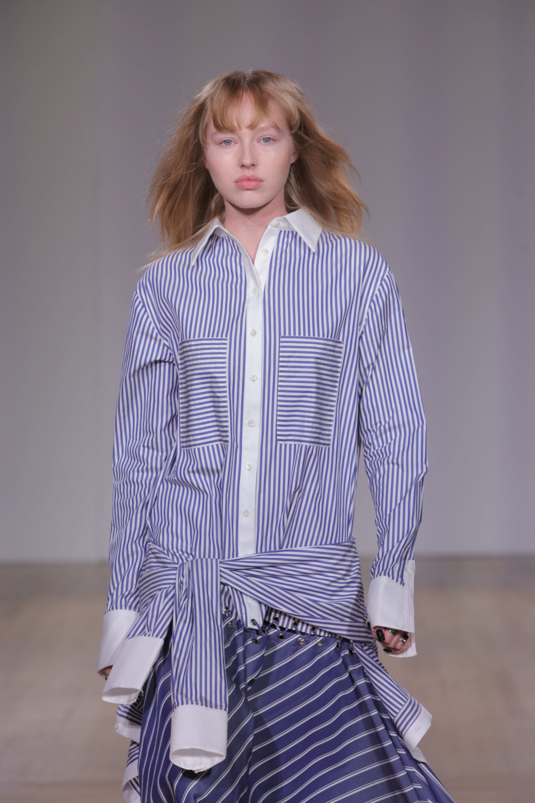 A model walking the runway wearing a blue pinstriped shirt and matching pants.