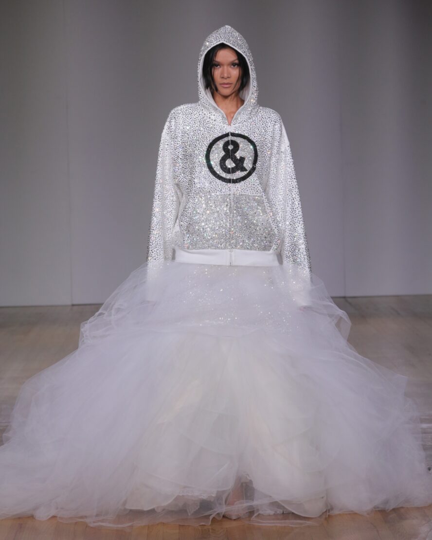 A model walking the runway wearing a white embellished hoodie and big puffy white skirt.