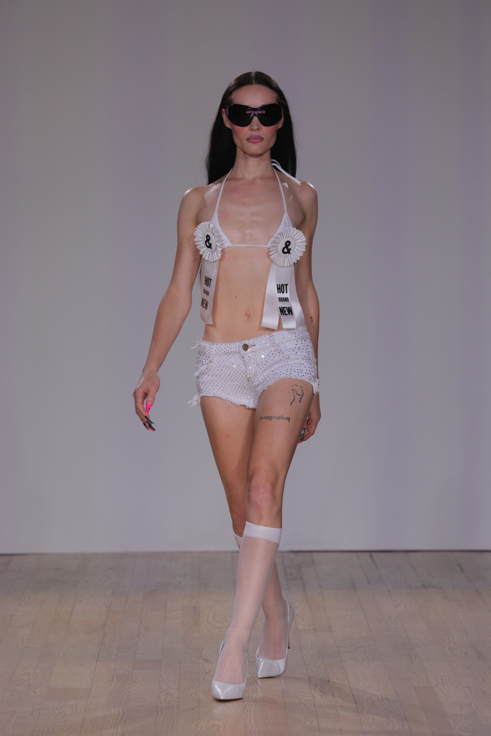 A model walking the runway wearing a white bikini top and white shorts.