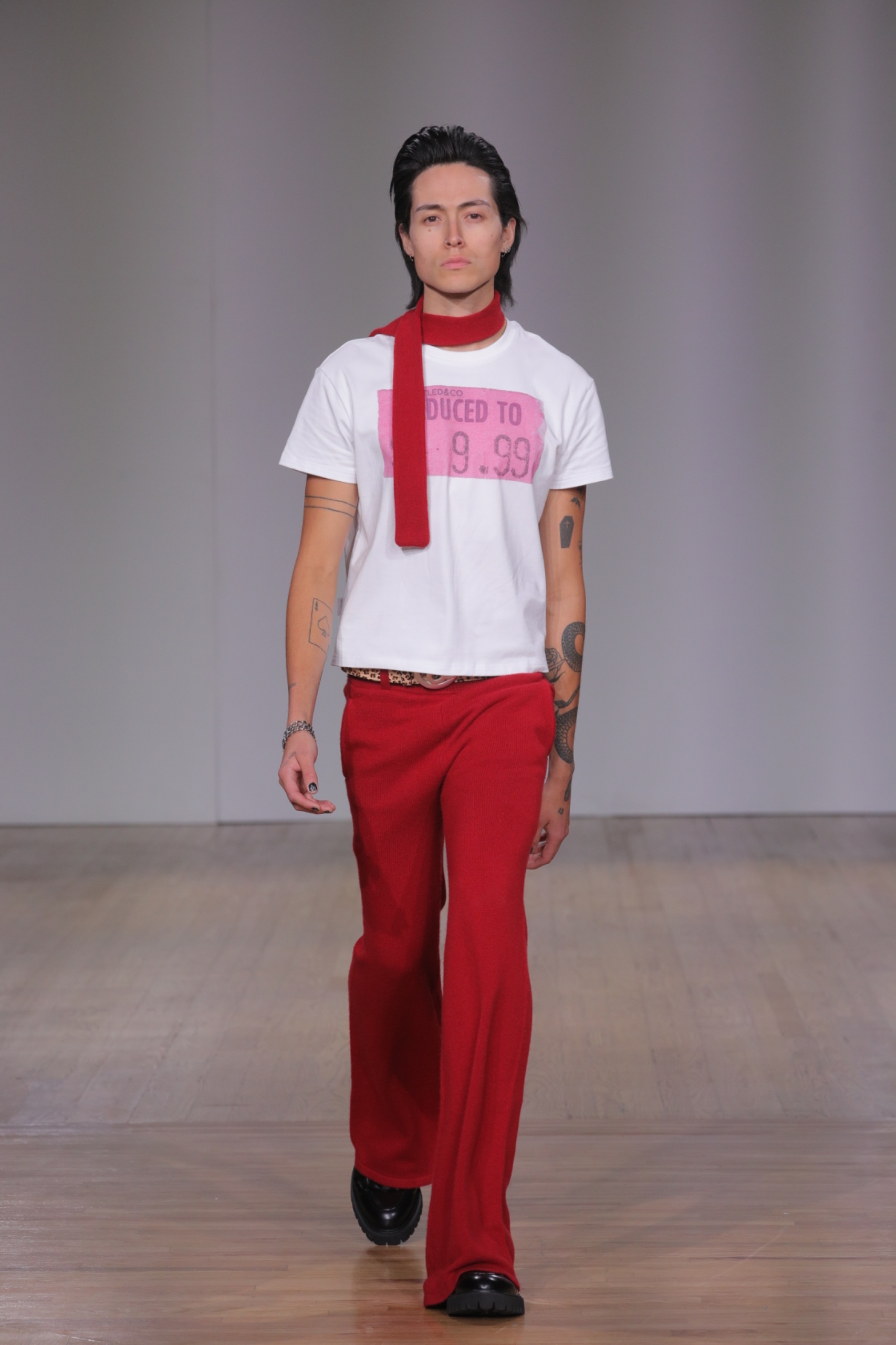 A model walking the runway wearing a red scarf, red pants and white t-shirt with pink detailing.