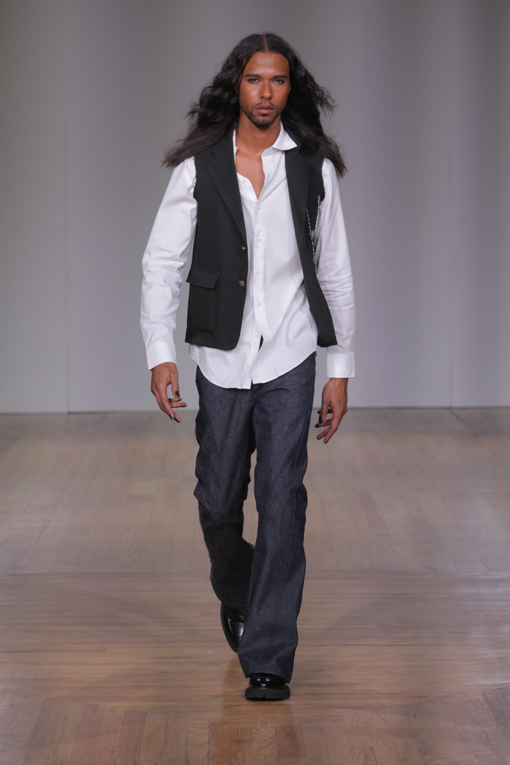 A model walking the runway wearing a white shirt, black waistcoat and pants.