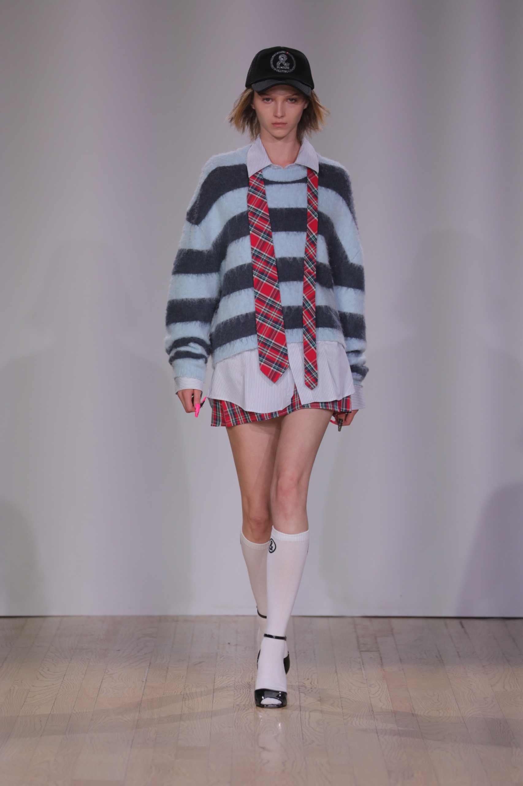 A model walking the runway wearing a blue striped jumper, a tartan tie and shorts.