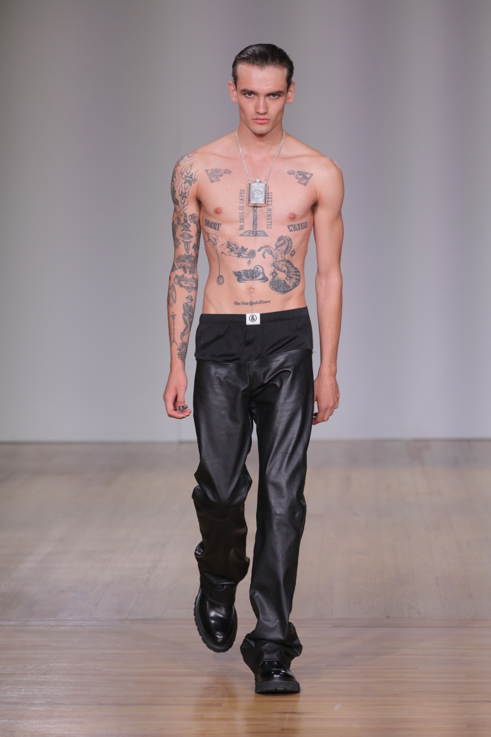 A model walking the runway wearing black pants and a necklace.