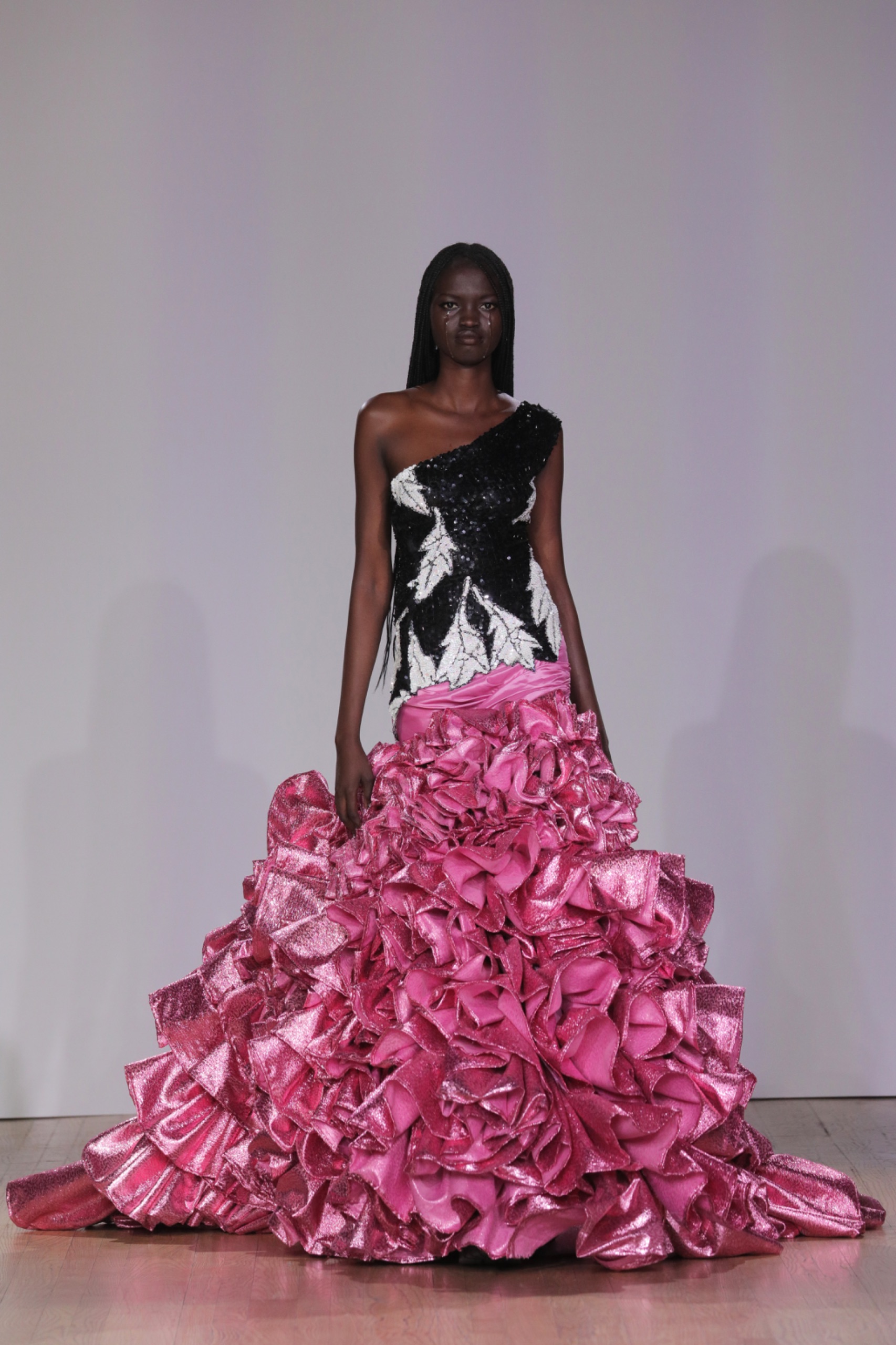 A model walking the runway wearing a white and black dress with pink embellishments.