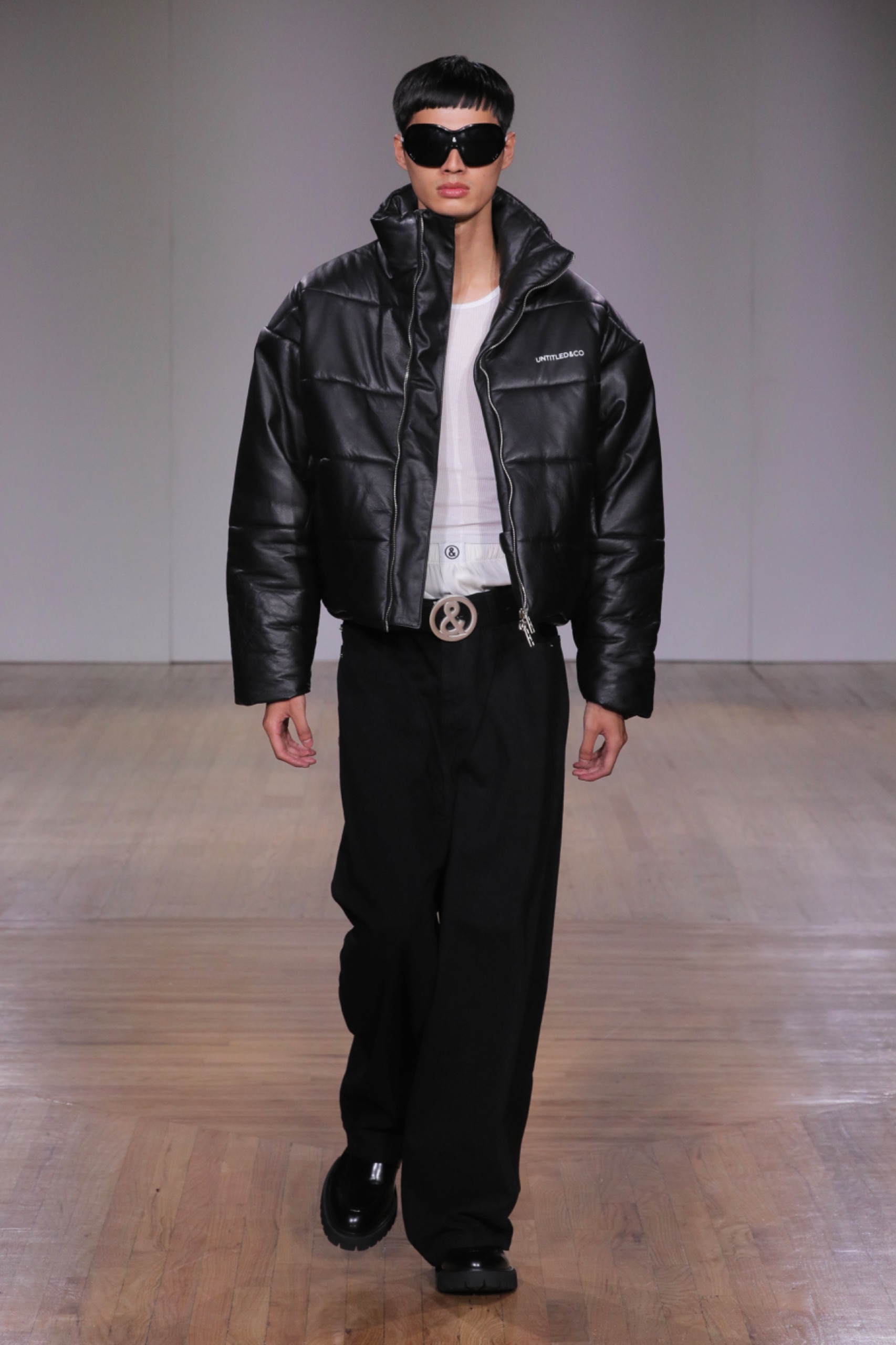 A model walking the runway wearing a white top, black jacket and black pants.