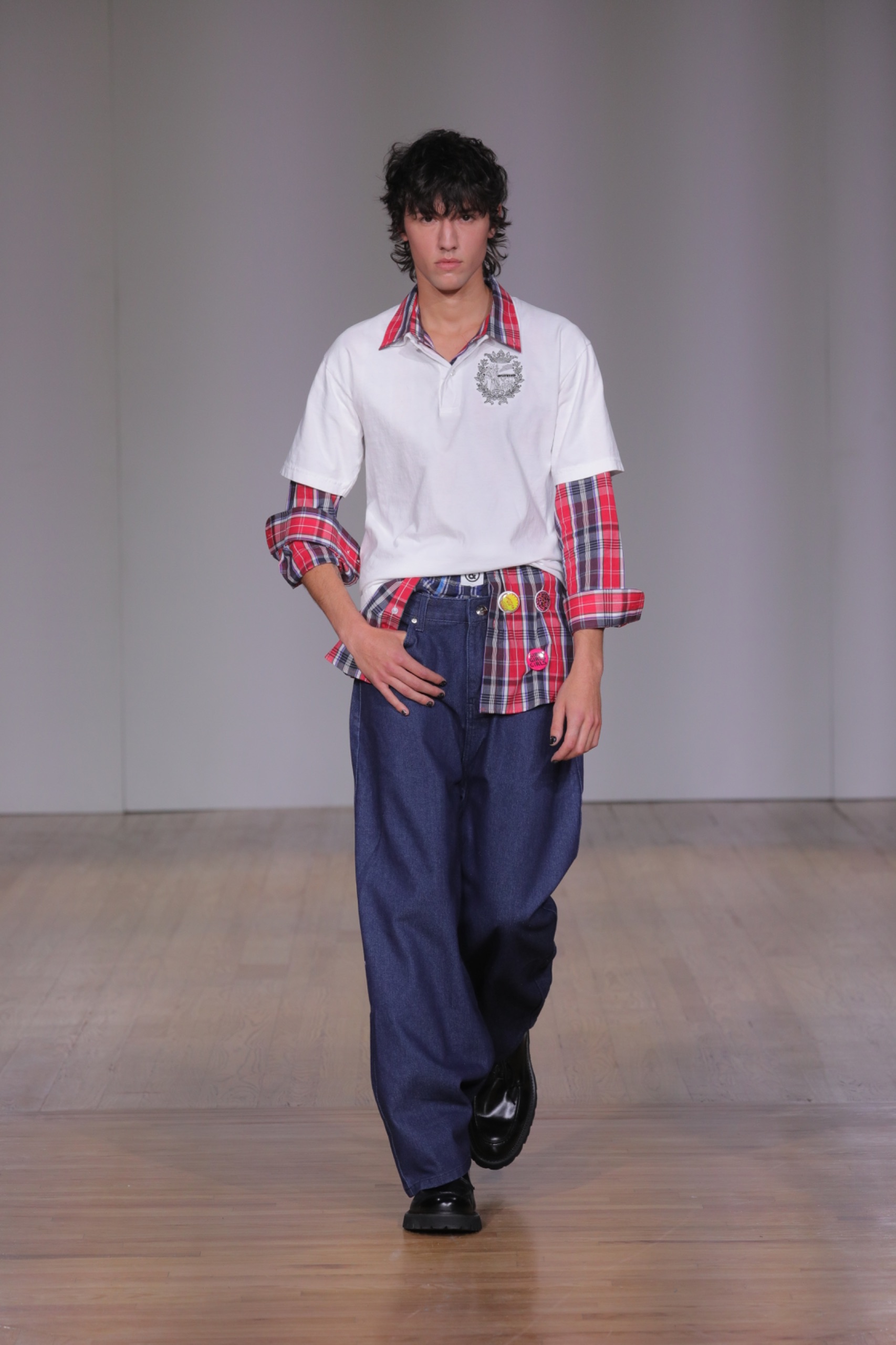 A model walking the runway wearing a tartan shirt, white t-shirt and dark blue jeans.