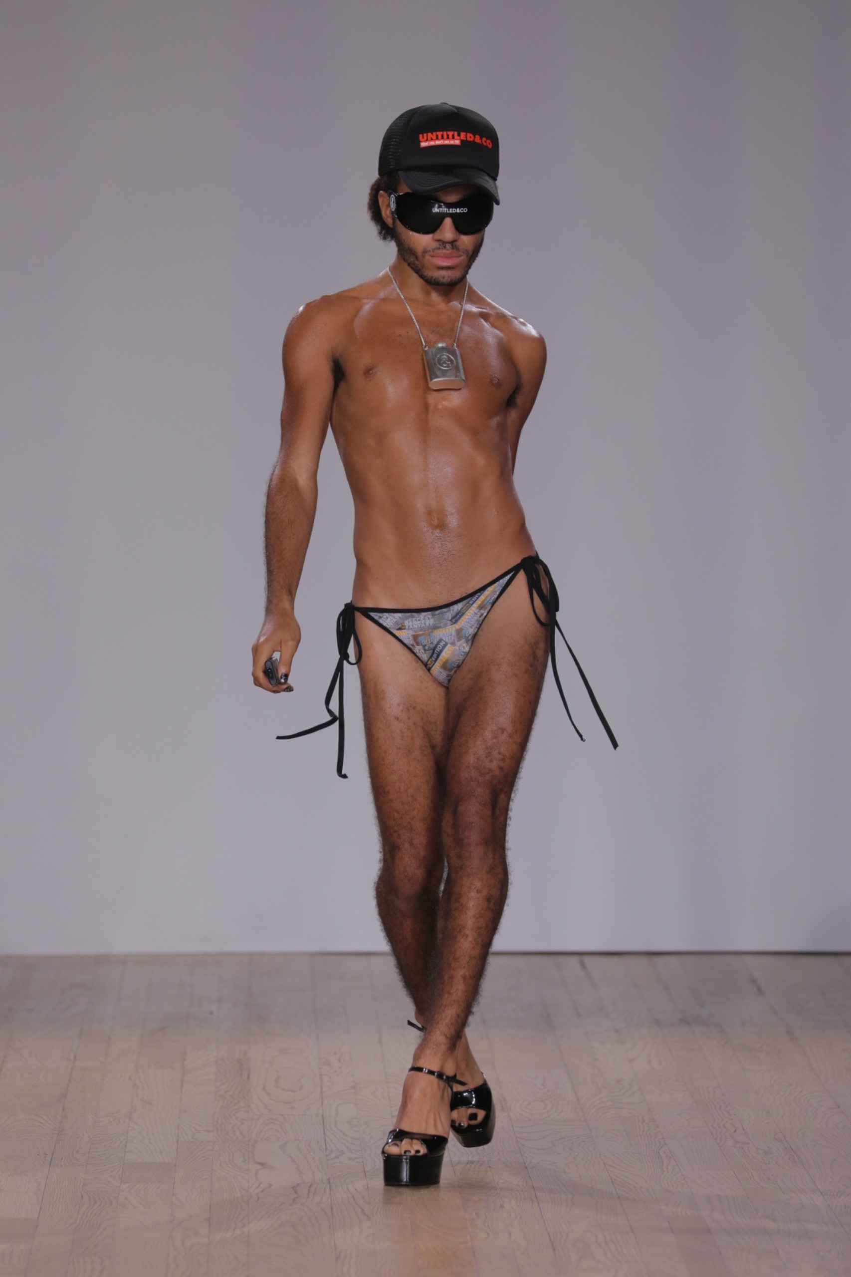 A model walking the runway wearing bikini bottom, sunglasses and a hat.