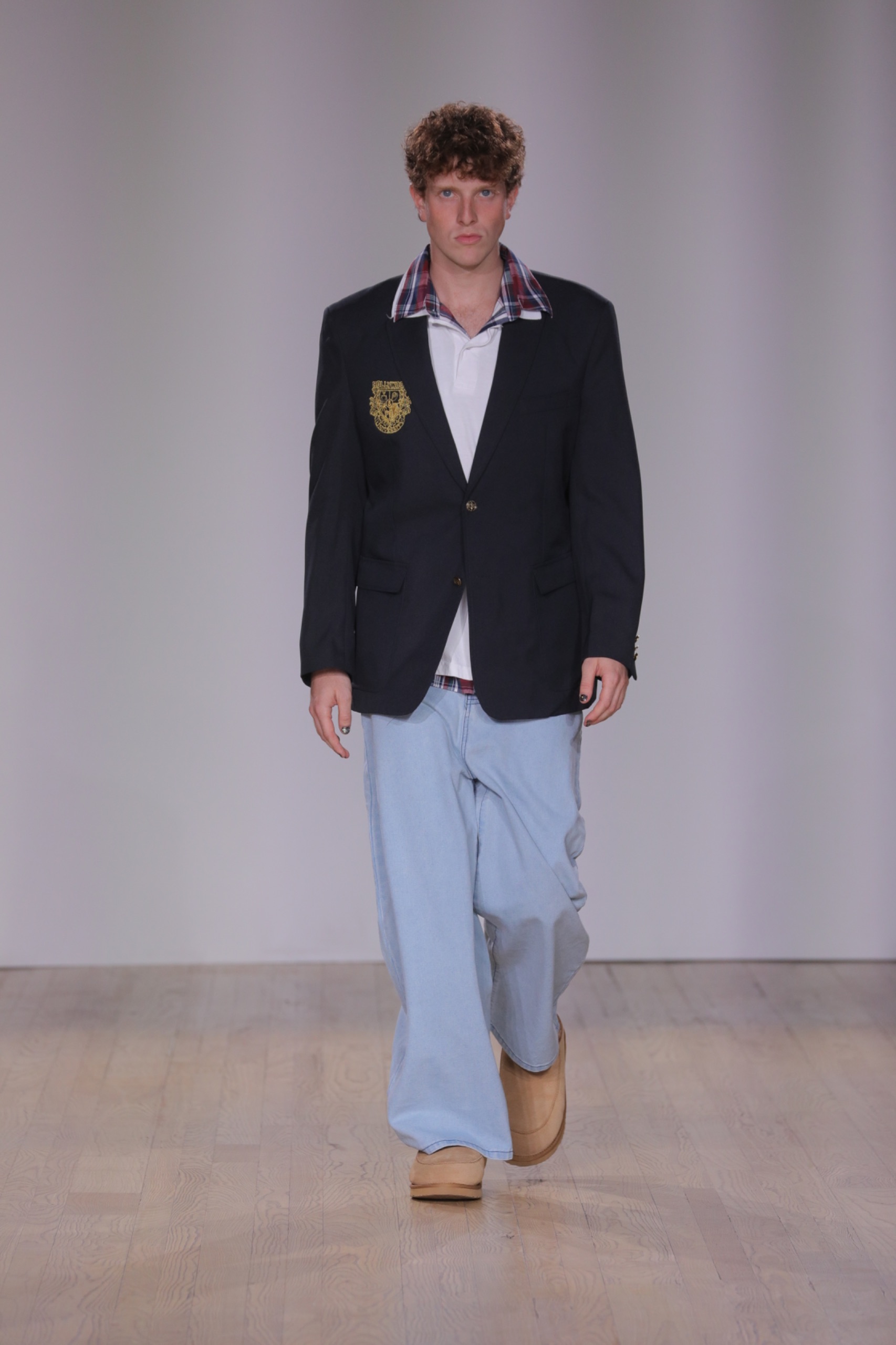 A model walking the runway wearing a black blazer, white top, light blue jeans and beige shoes.