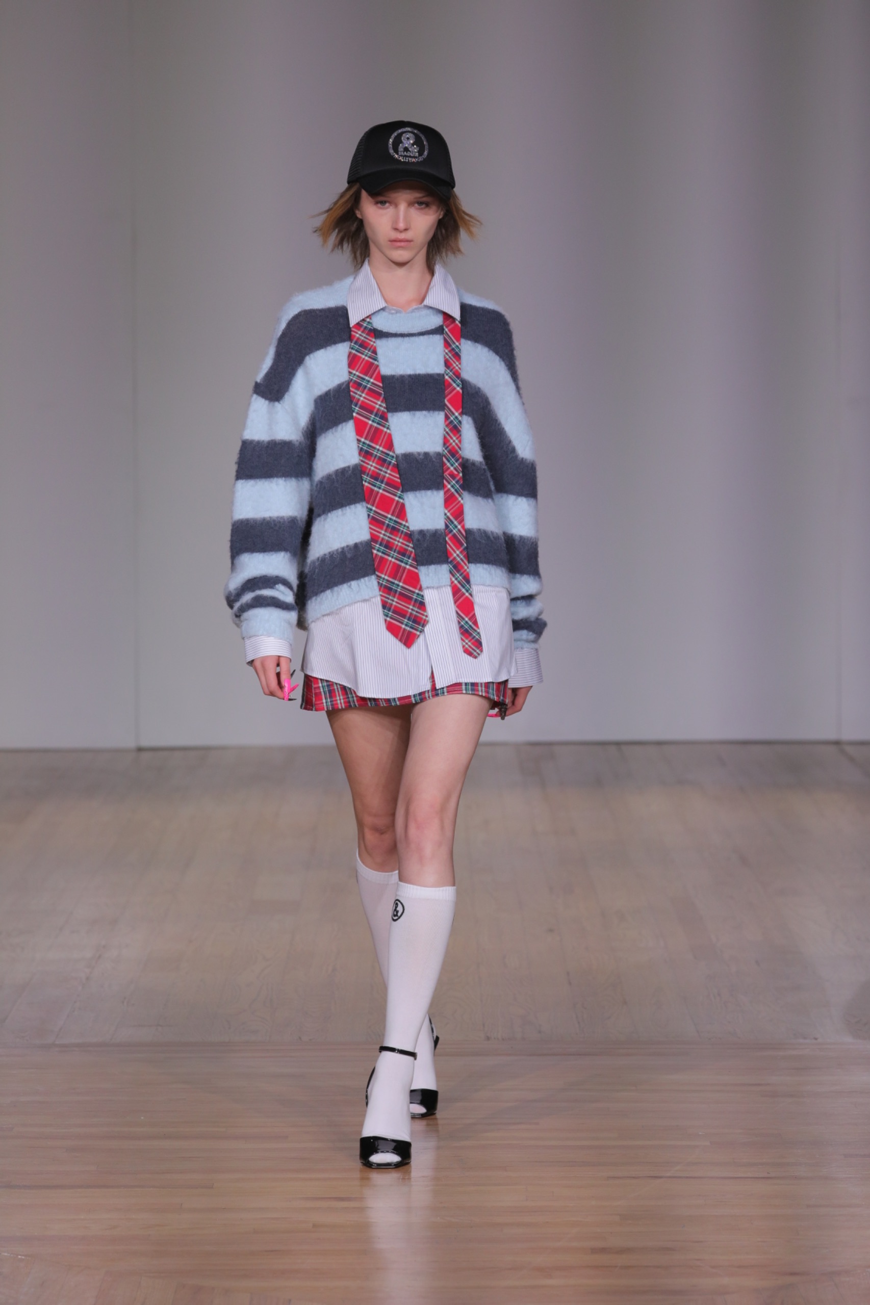 A model walking the runway wearing a blue striped jumper, a tartan tie and shorts.