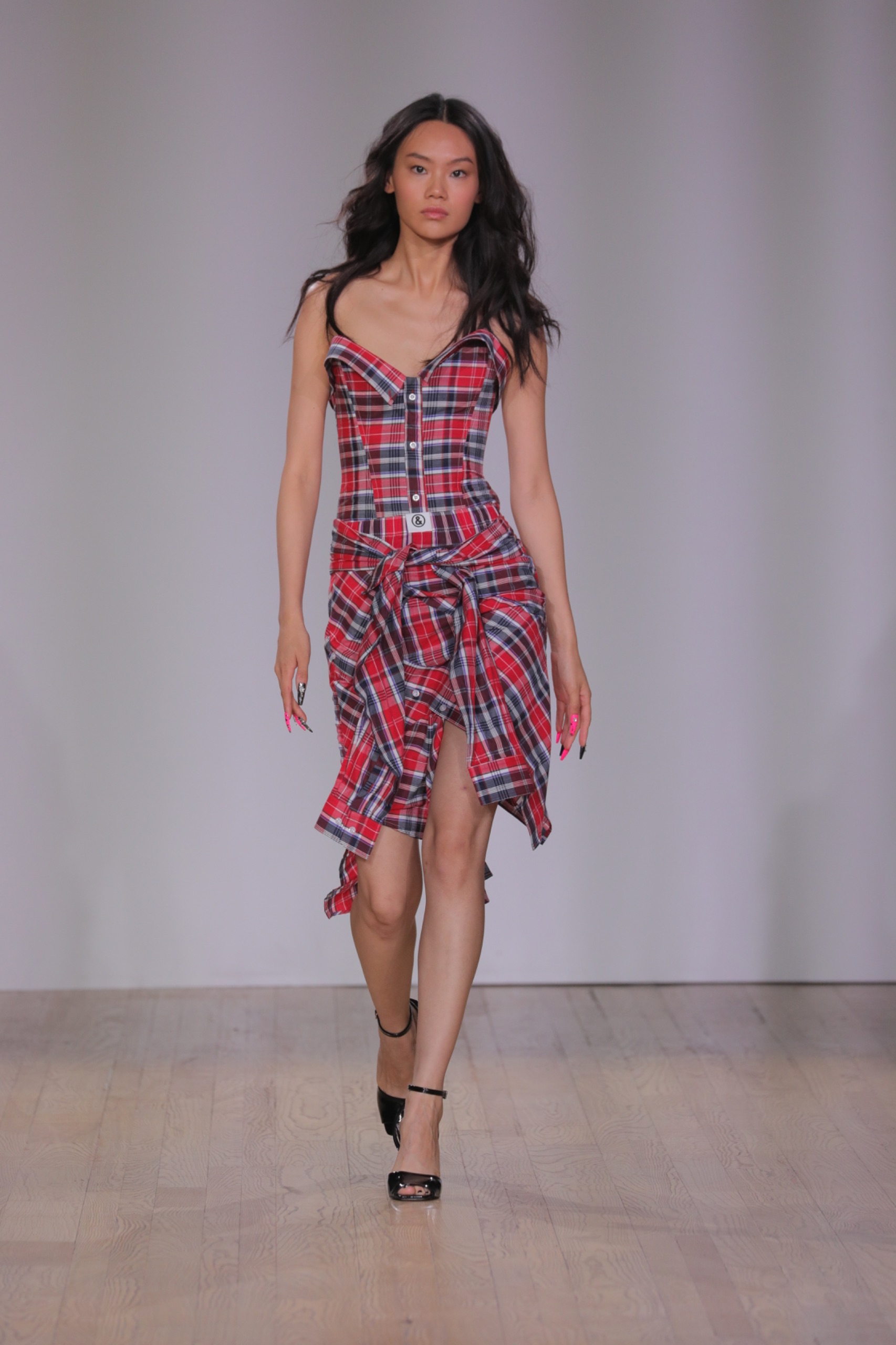 A model walking the runway wearing a red tartan dress.