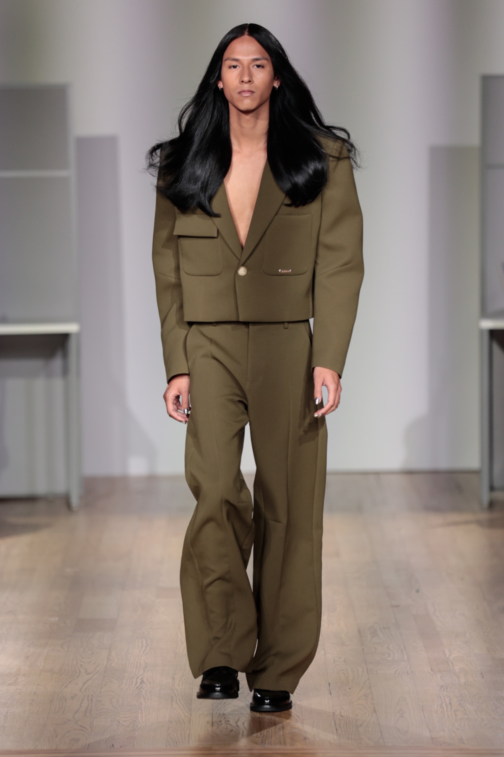 A model walking the runway wearing an olive green blazer and matching trousers.