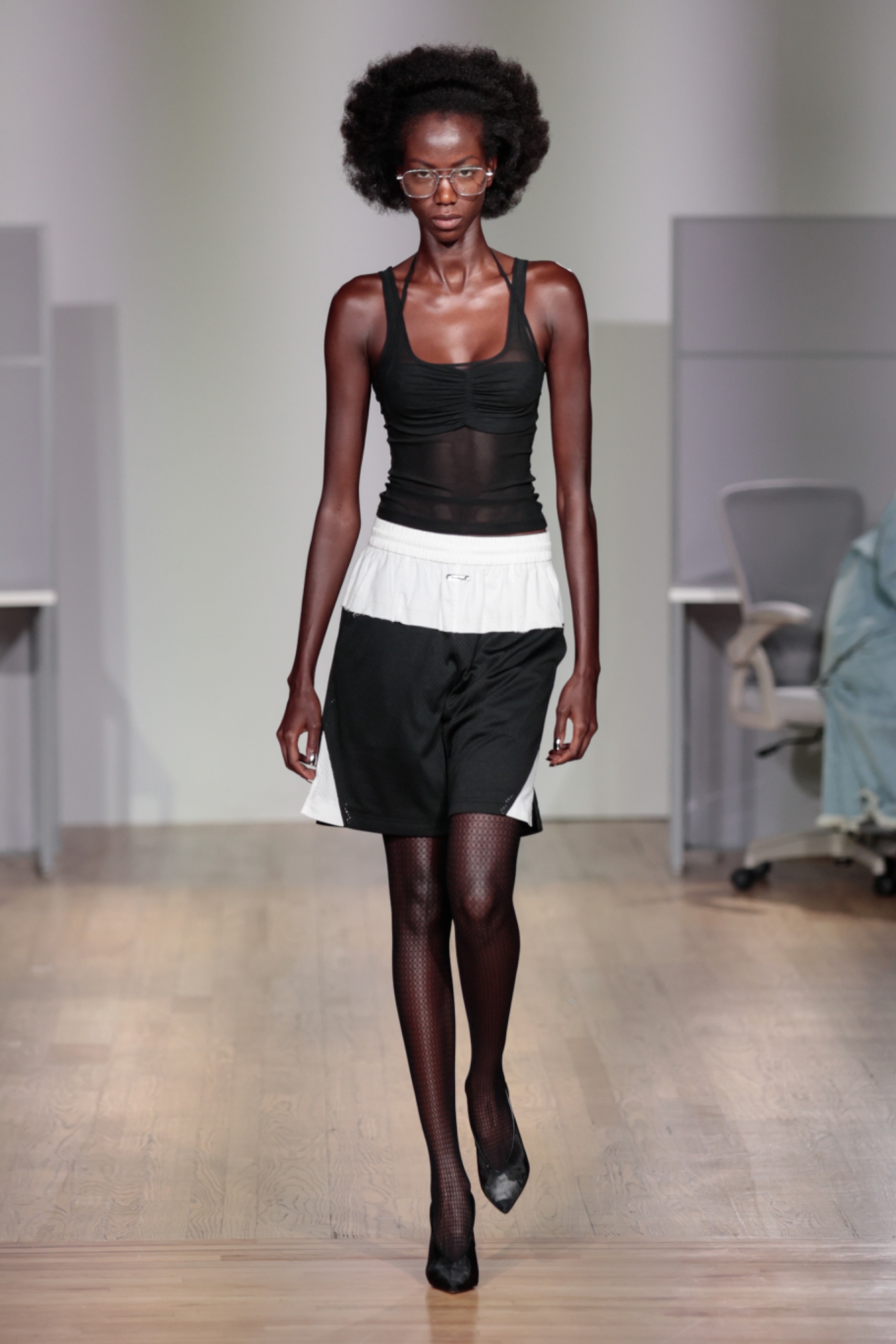 A model walking the runway wearing a black and white dress with black tights.