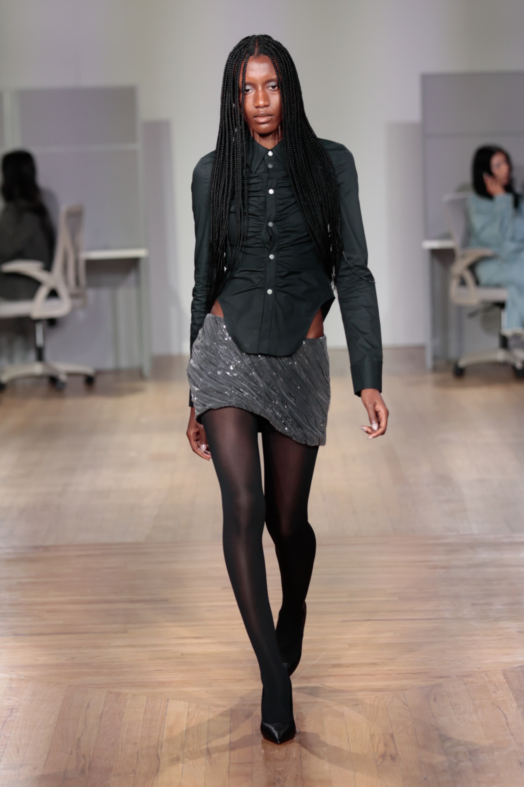 A model walking the runway wearing a dark grey cardigan, skirt and tights.