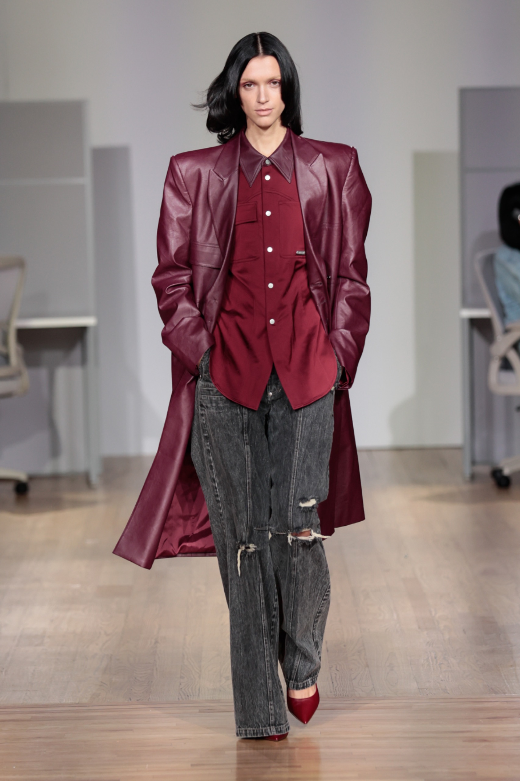 A model walking the runway wearing a red shirt, jacket and black pants.