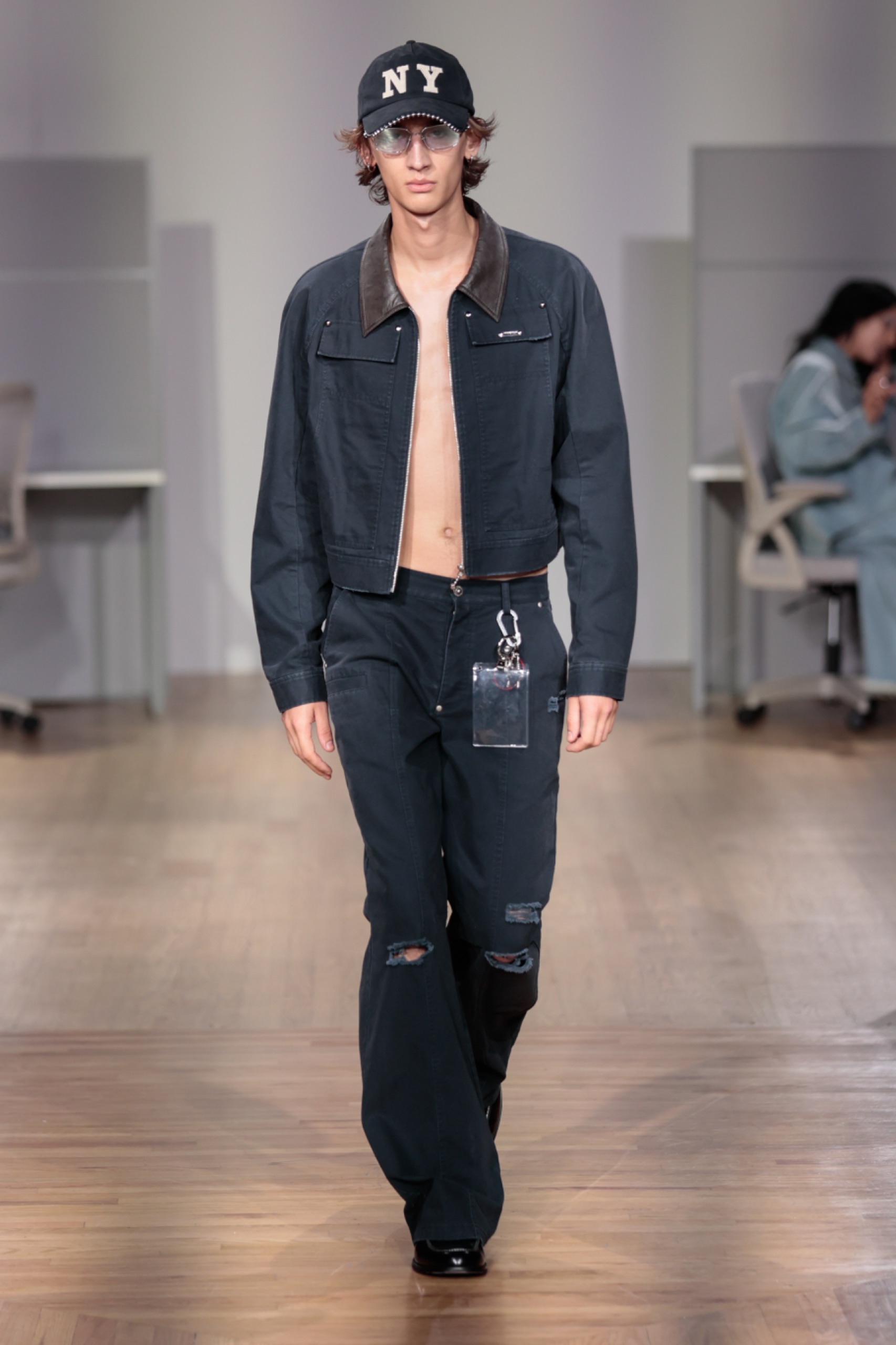 A model walking the runway wearing a black cap, jacket and pants.