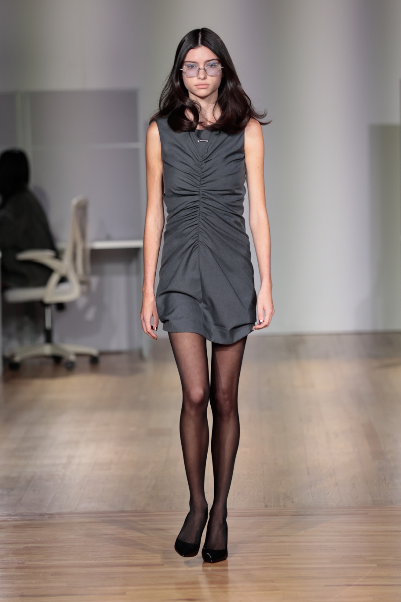 A model walking the runway wearing a grey dress and black tights.