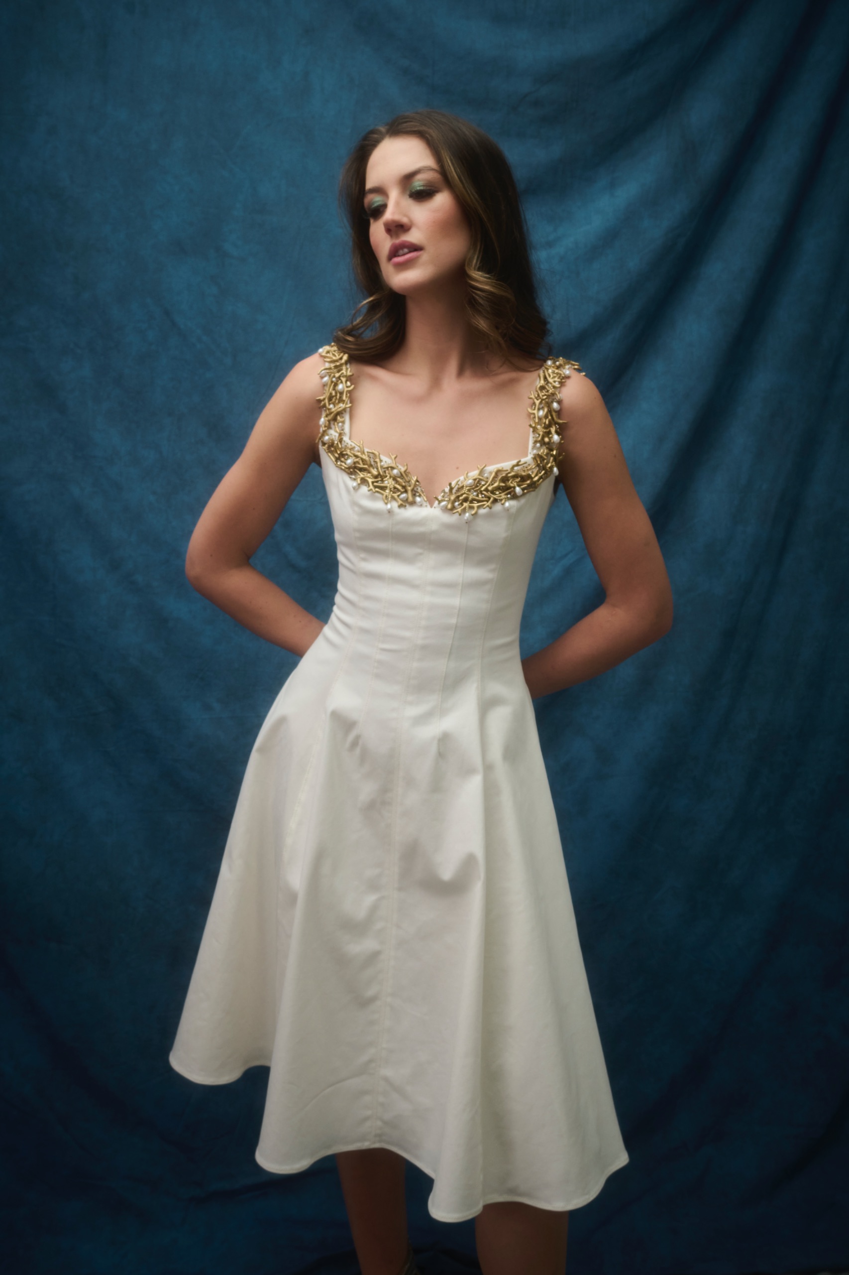 A model wearing a white dress with gold detailing.