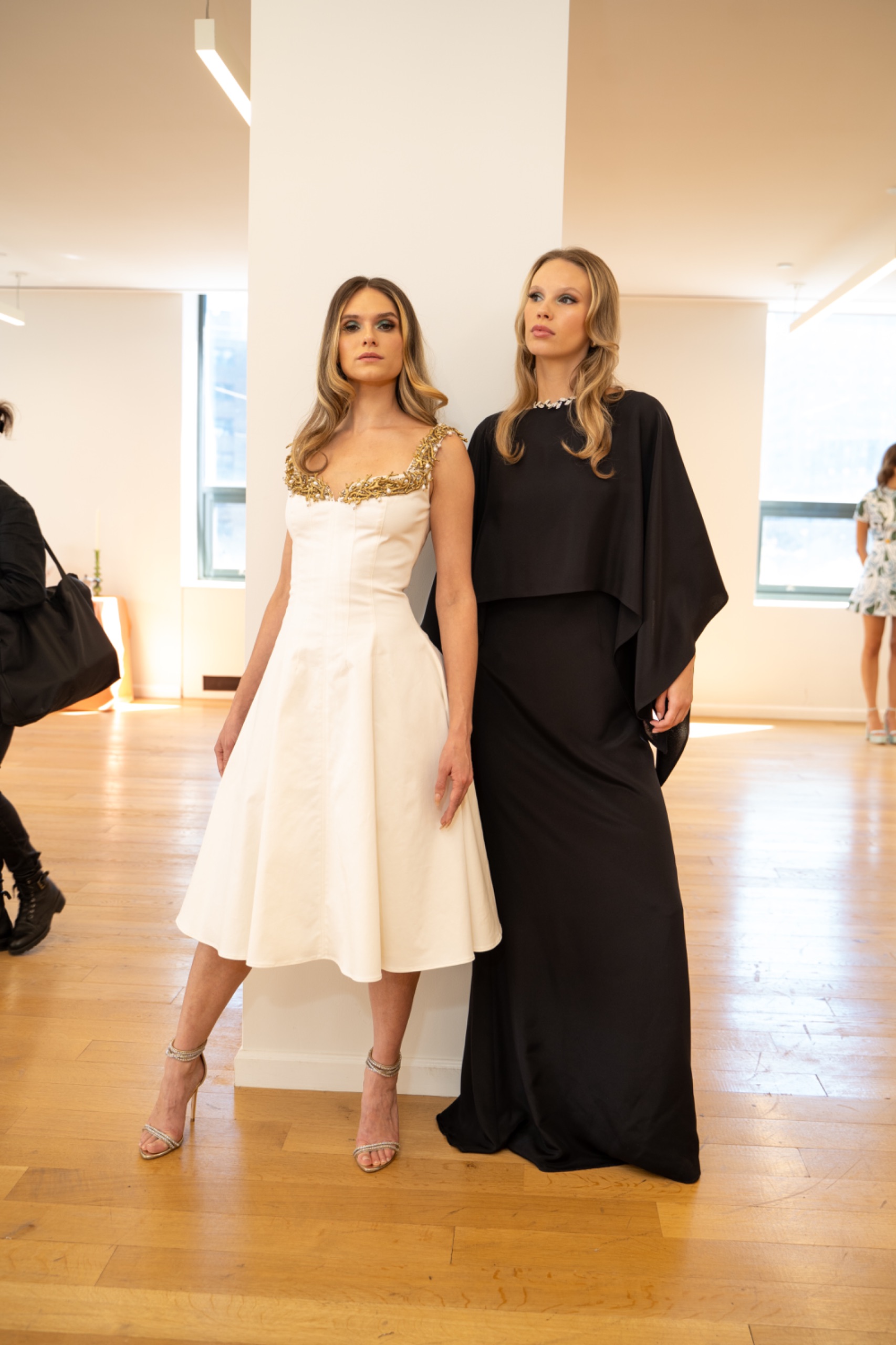 2 models. The model on the left is wearing a long white dress. The model on the right is wearing a long black dress.