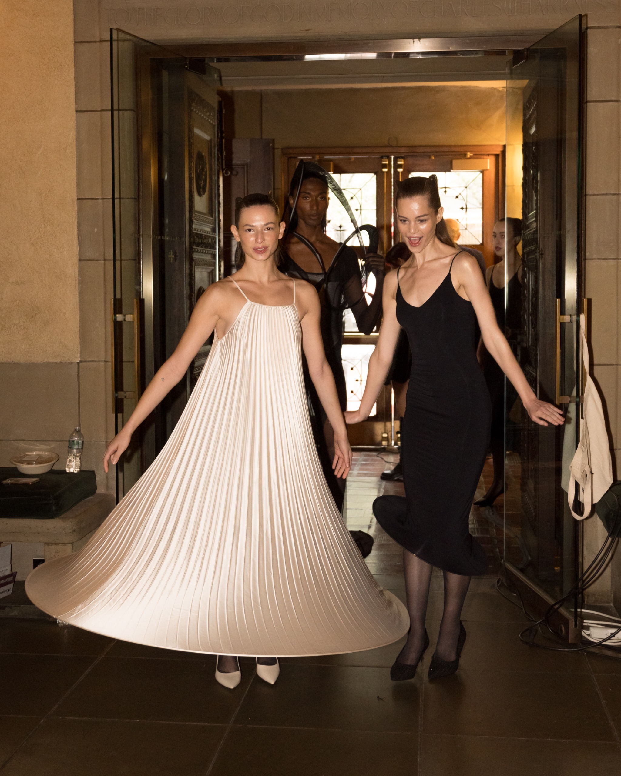 Two models wearing long dresses, one black and one pale tint.