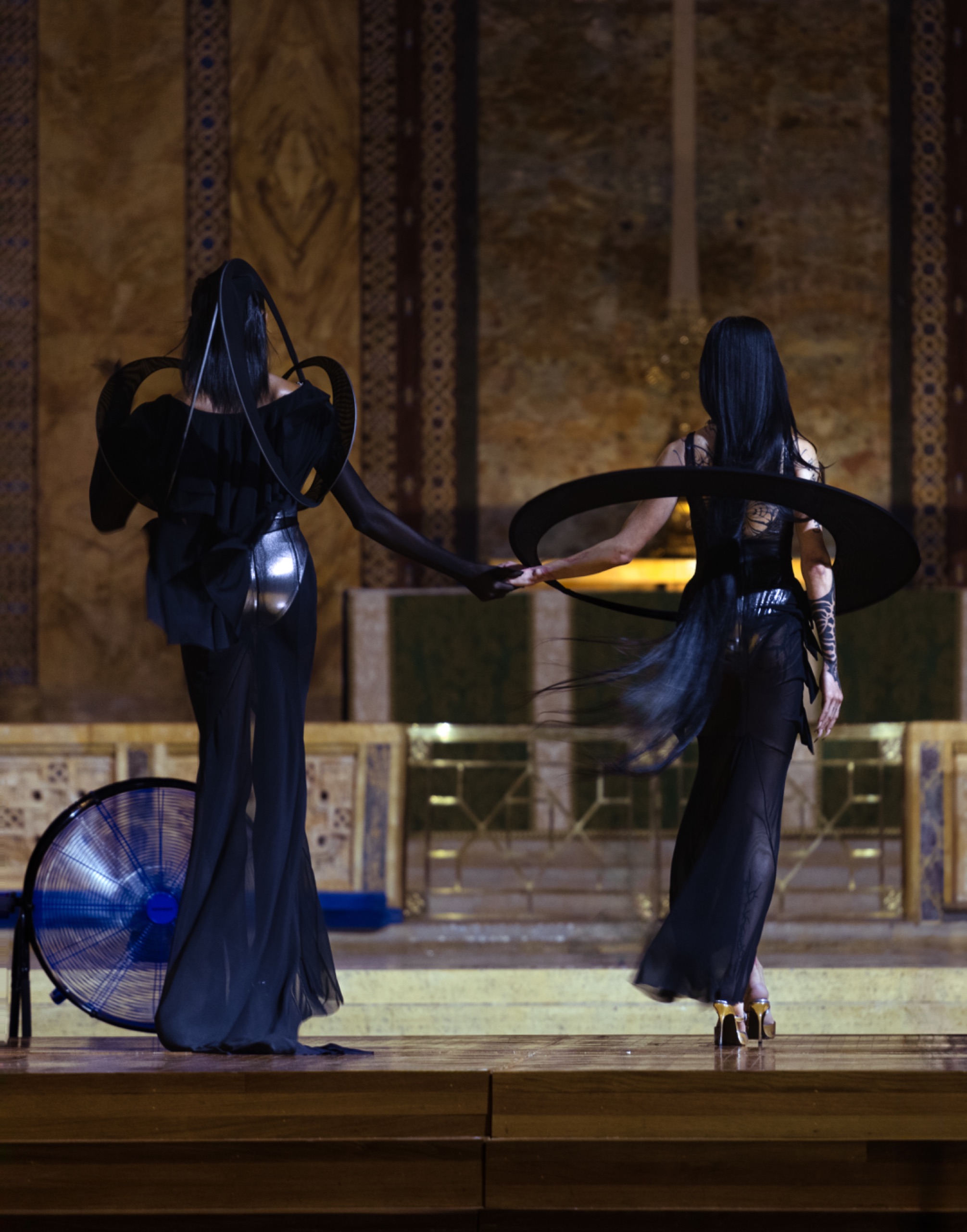 Two models holding hands while wearing long black dresses with purple details.