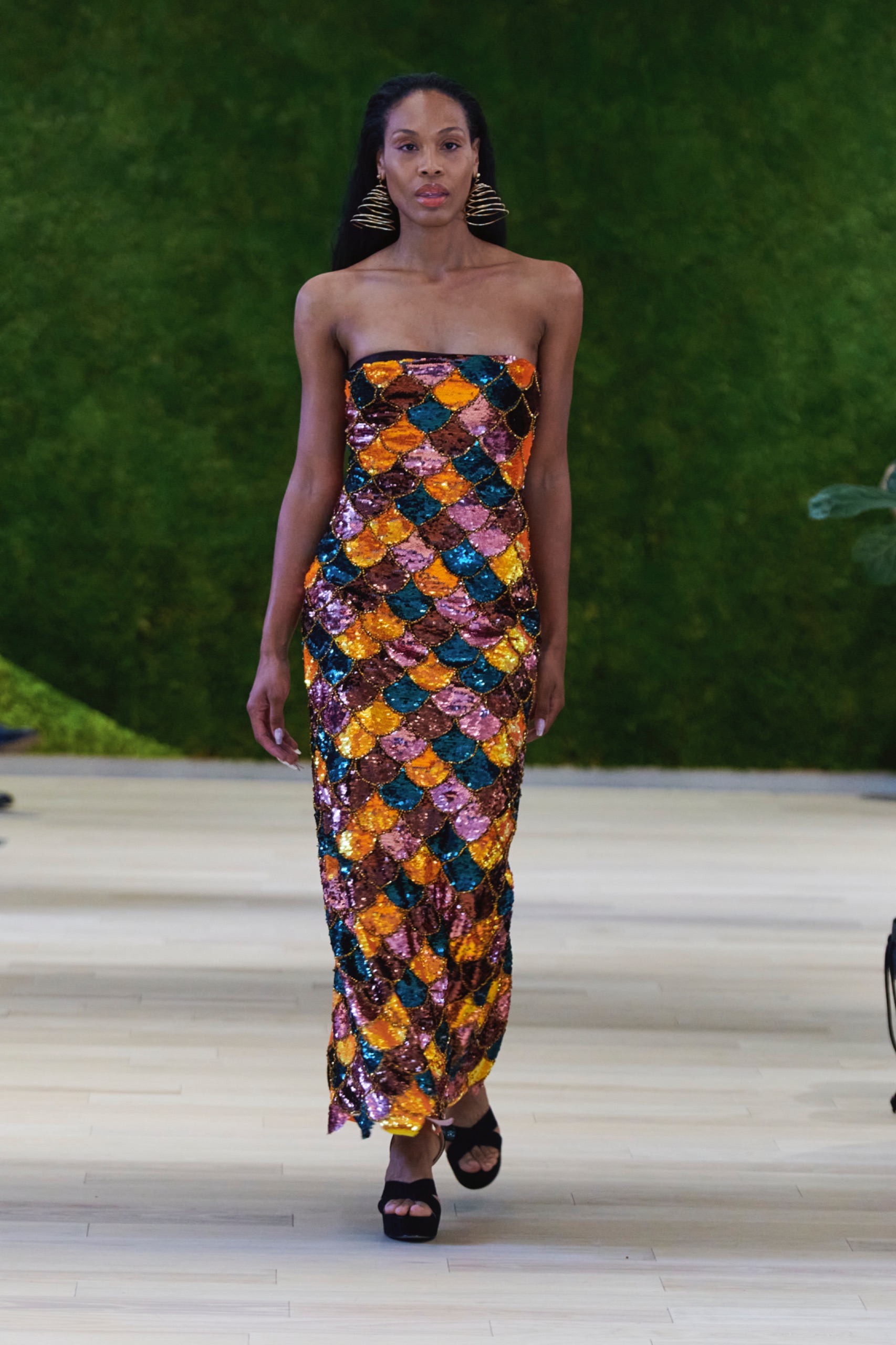 A model walking the runway wearing a orange abstract pattern dress.