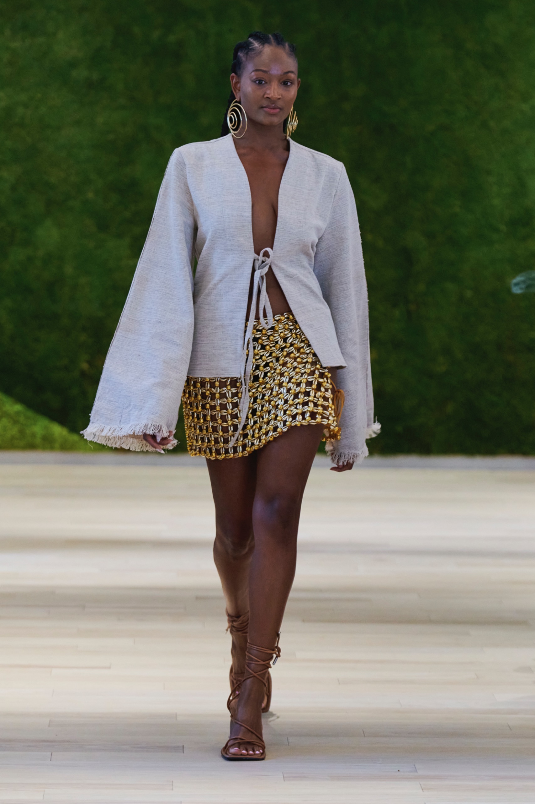 A model walking the runway wearing a white jacket and yellow patterned skirt.