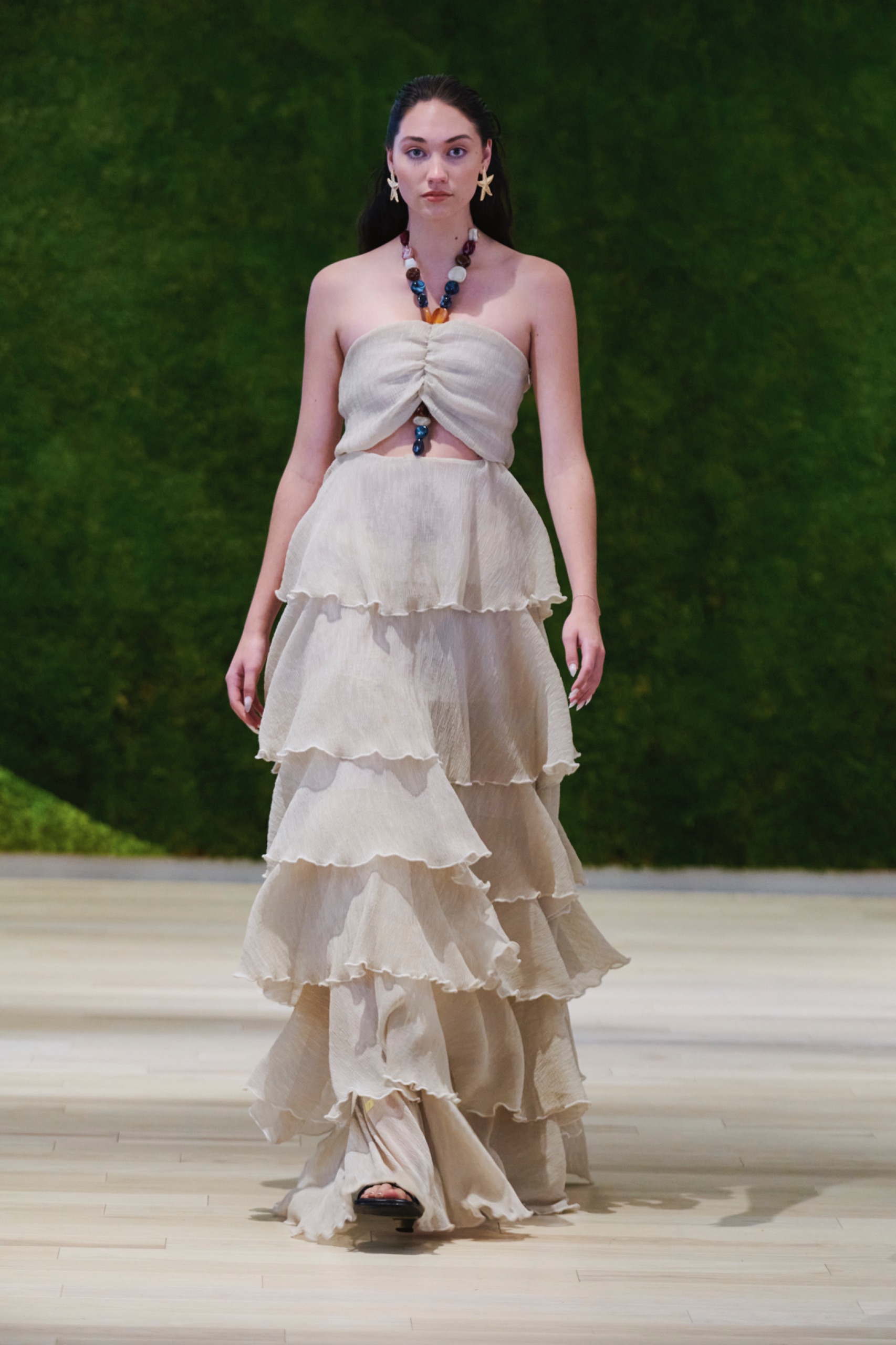 A model walking the runway wearing a long beige ruffle dress.