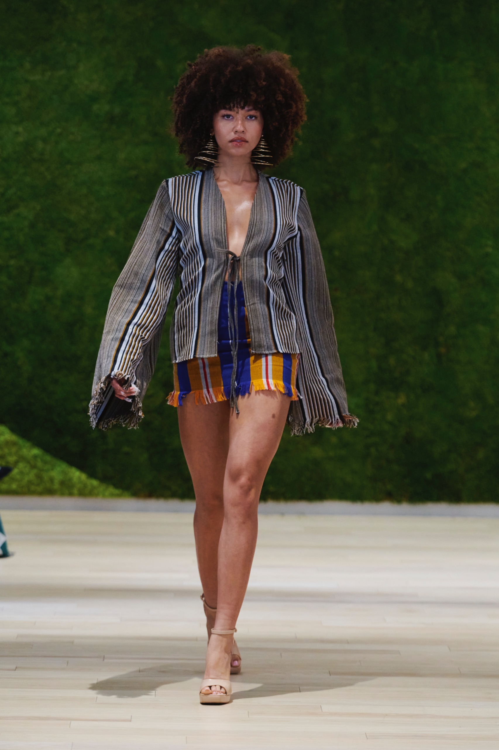 A model walking the runway wearing a grey striped jacket with orange shorts.