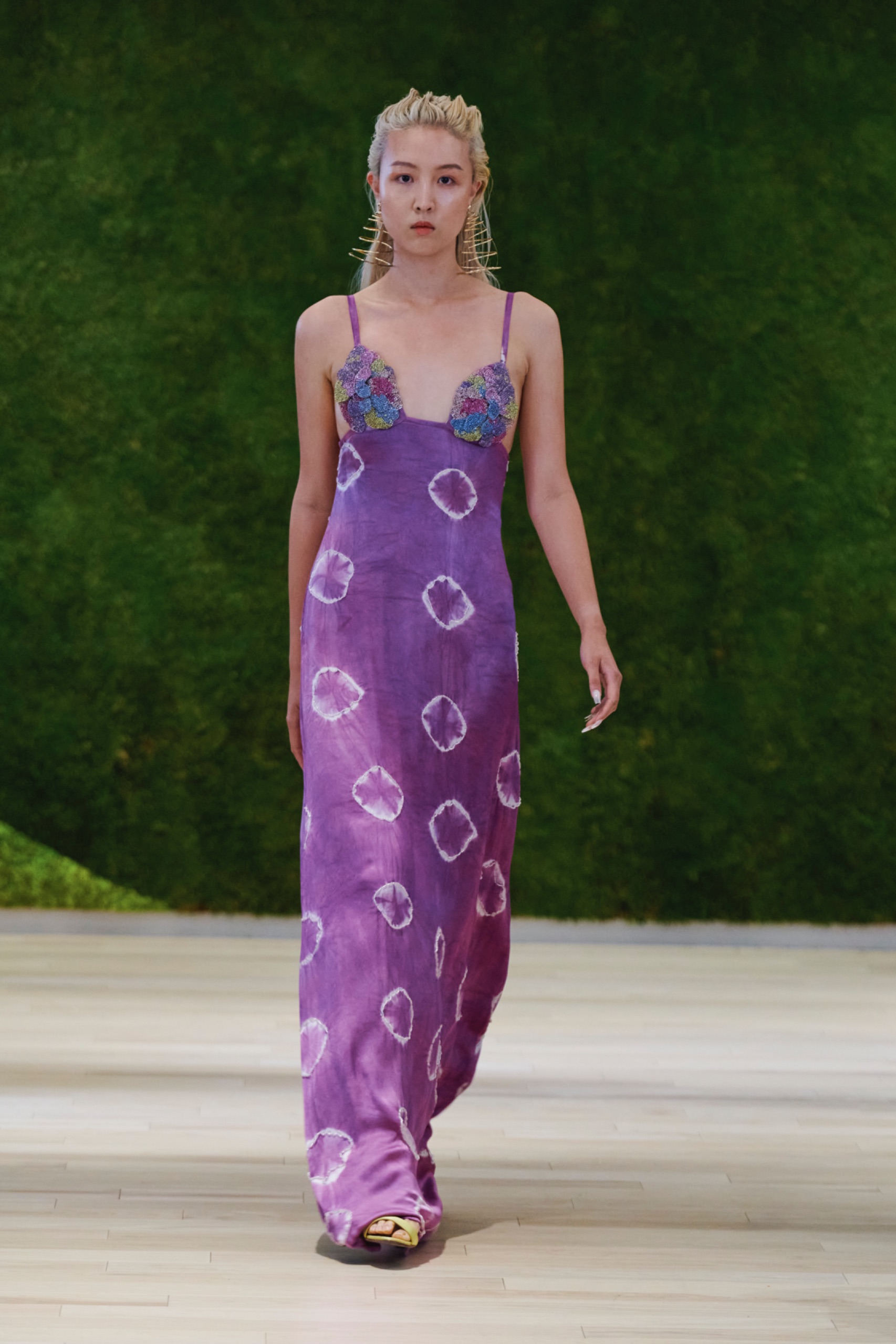 A model walking the runway wearing a long purple dress with swirled pattern.