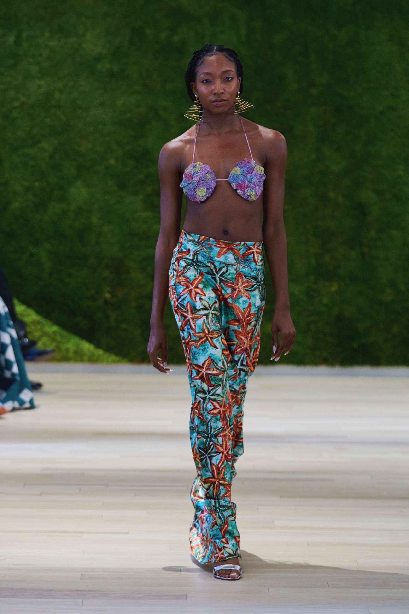 A model walking the runway wearing a purple top and colourful pants.