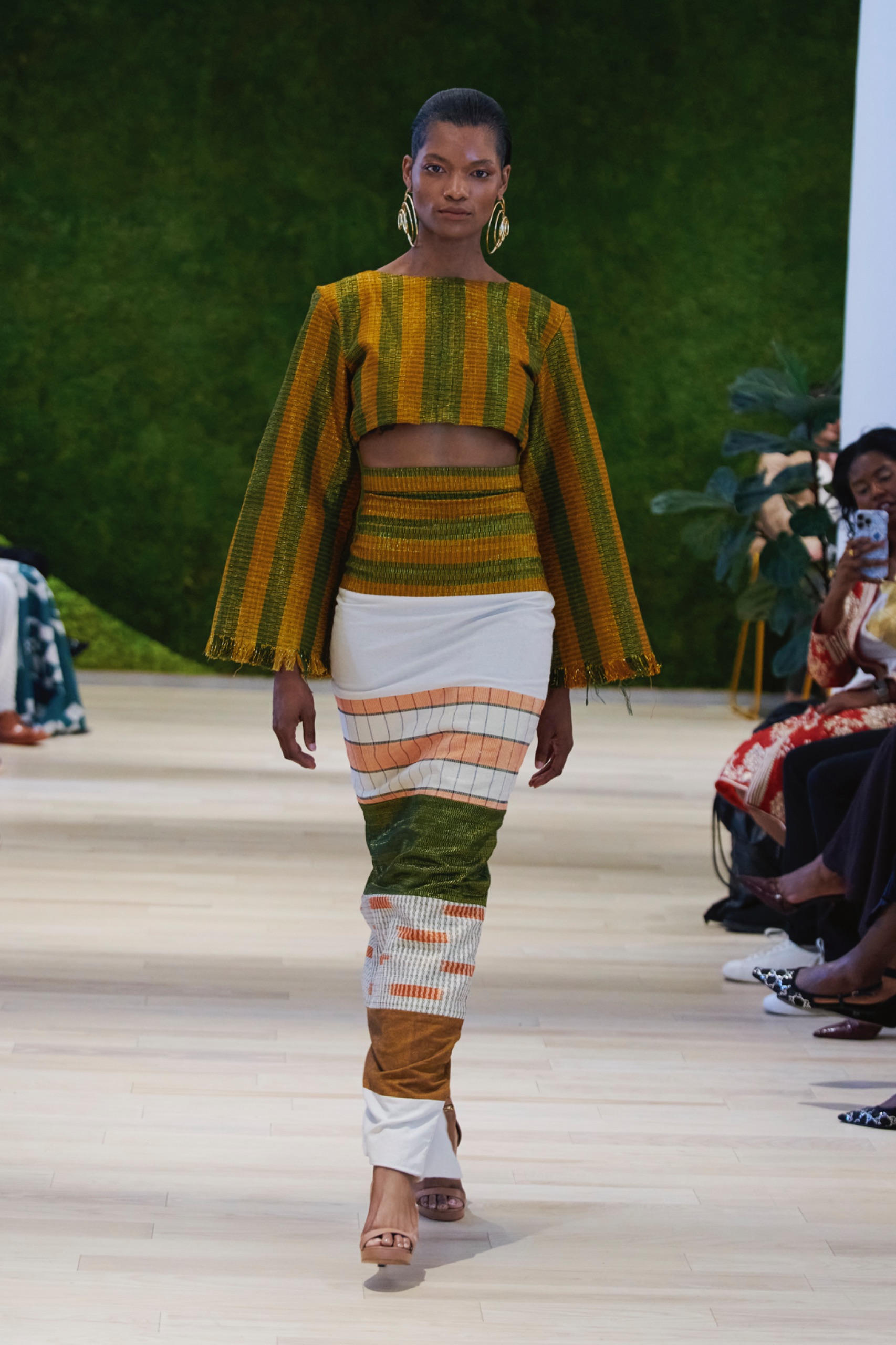 A model walking the runway wearing a yellow and green striped top and striped skirt.