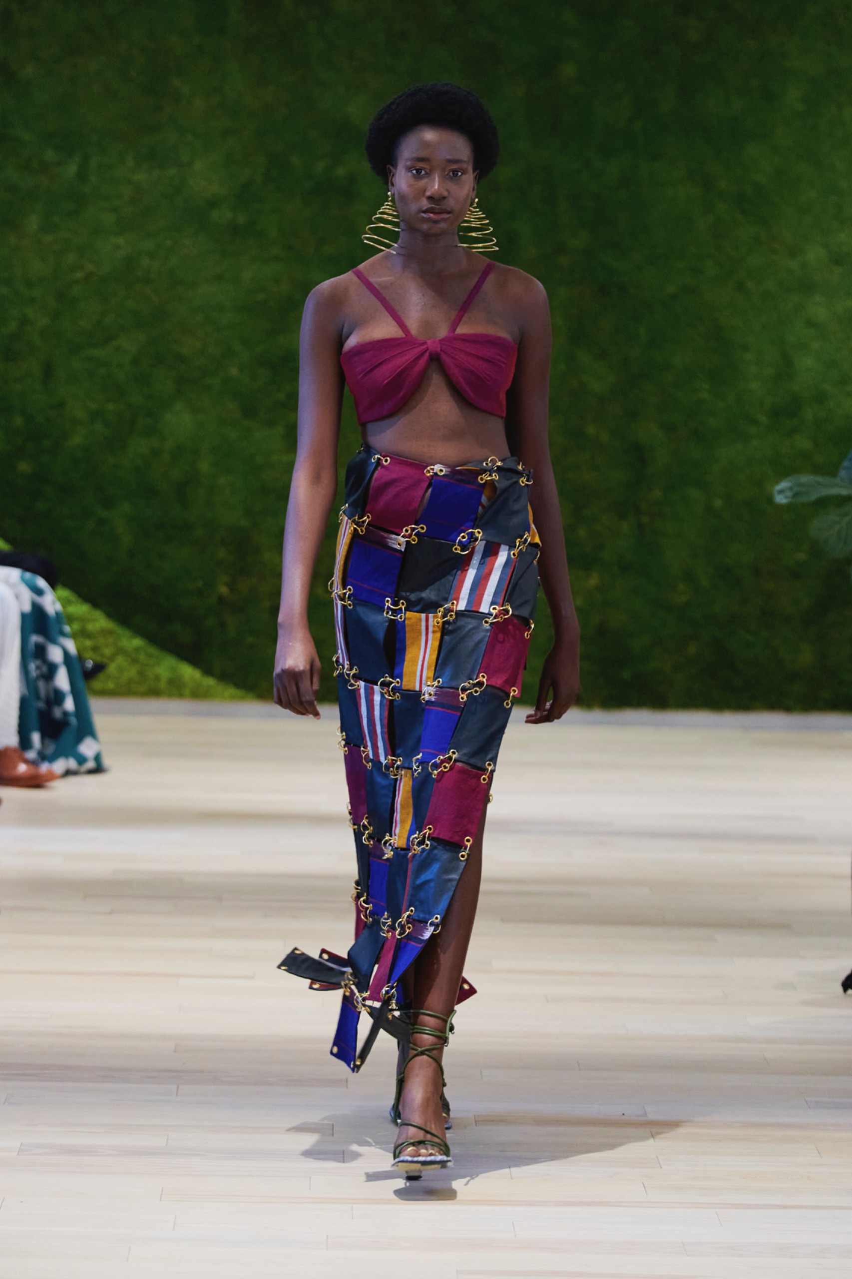 A model walking the runway wearing a purple top and colourful skirt.