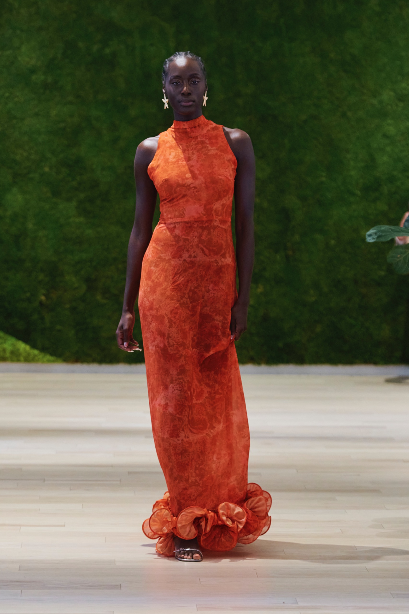 A model walking the runway wearing a long orange dress.