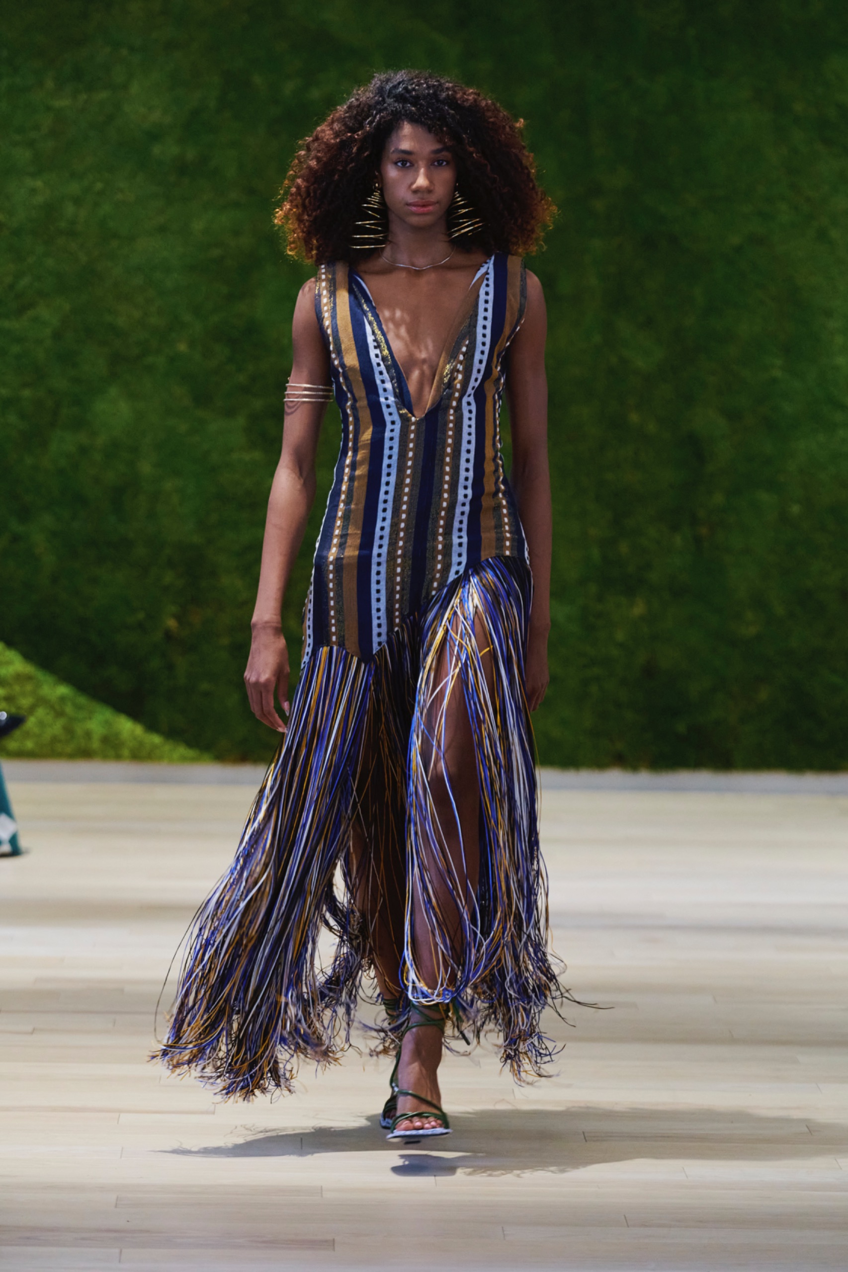 A model walking the runway wearing a striped colourful dress.