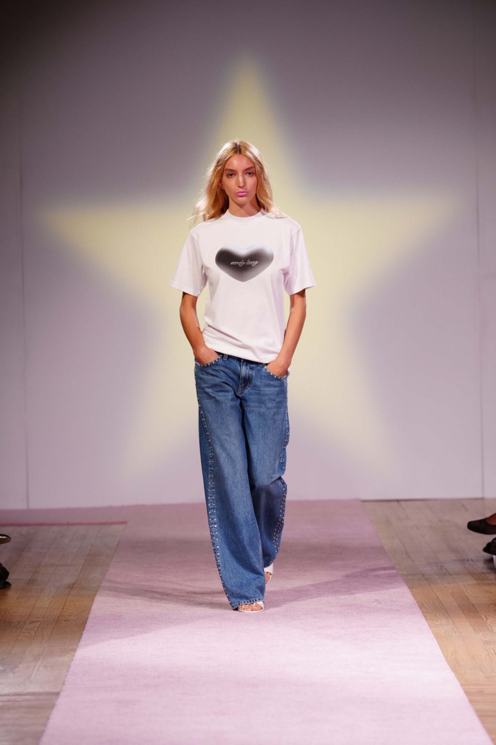 A model walking a runway wearing a white t-shirt with blue jeans.