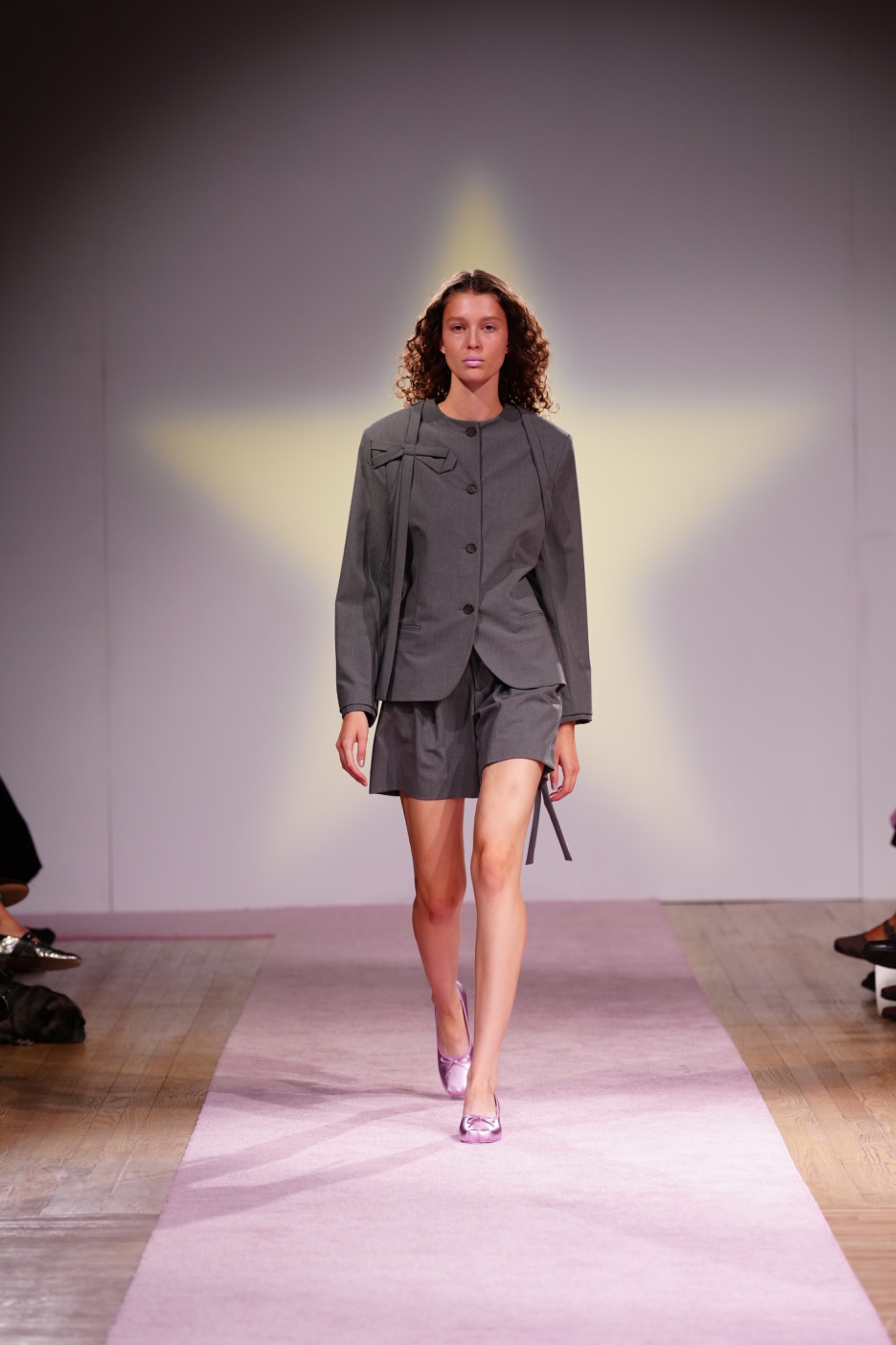 A model walking the runway wearing a grey blazer and skirt.