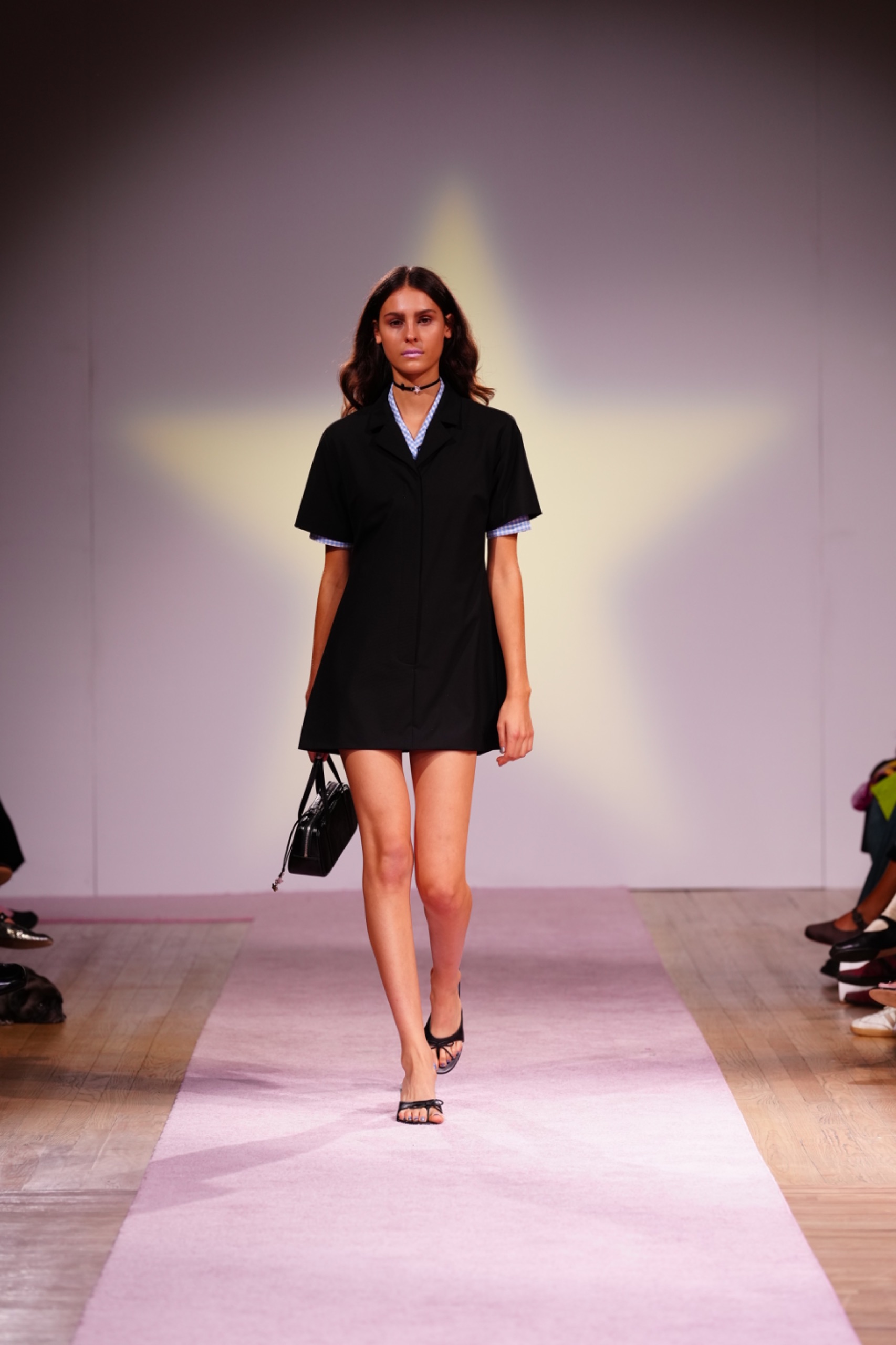 A model walking the runway wearing a black dress and black bag.