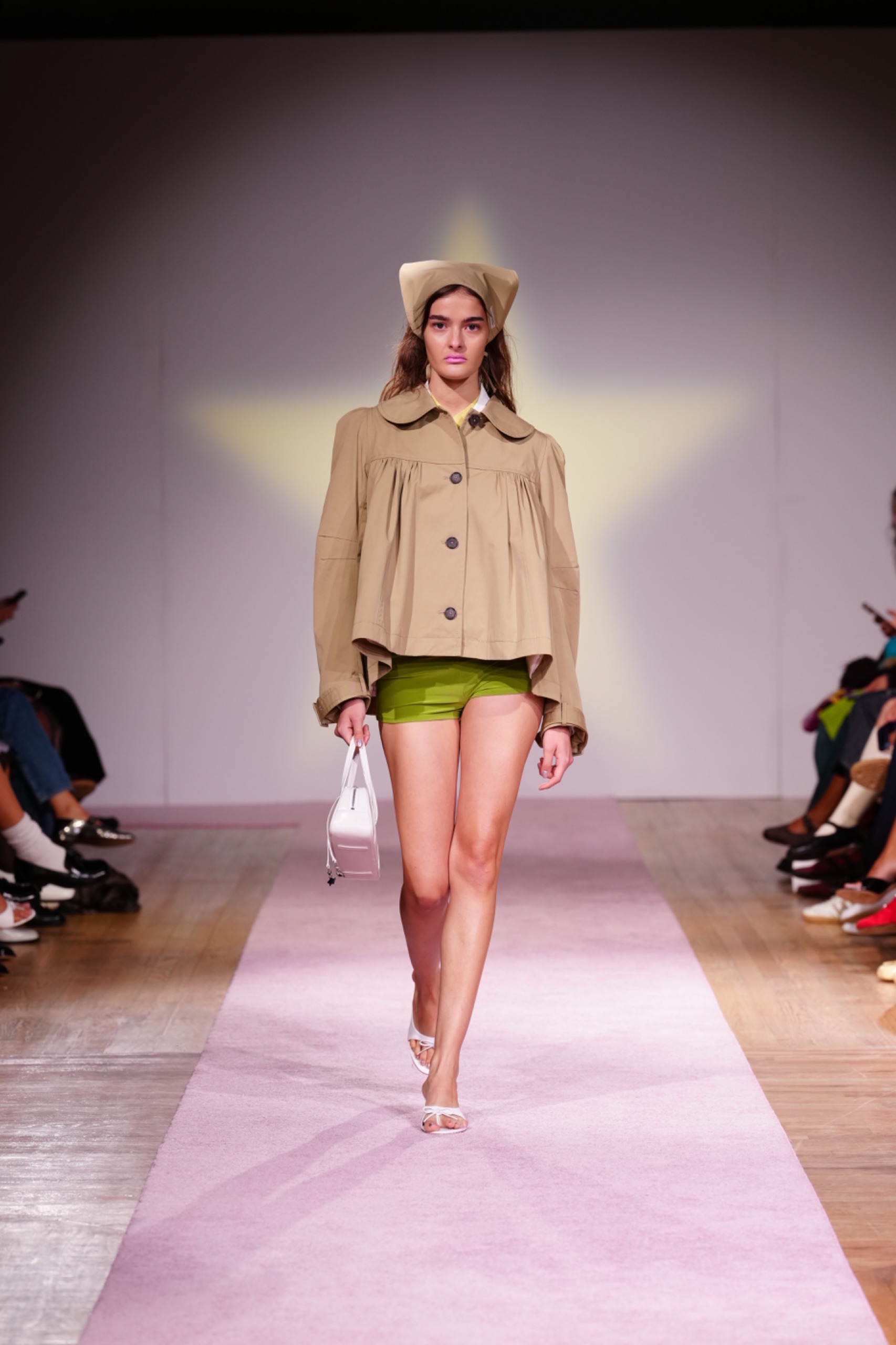 A model walking the runway wearing a beige jacket and green shorts.