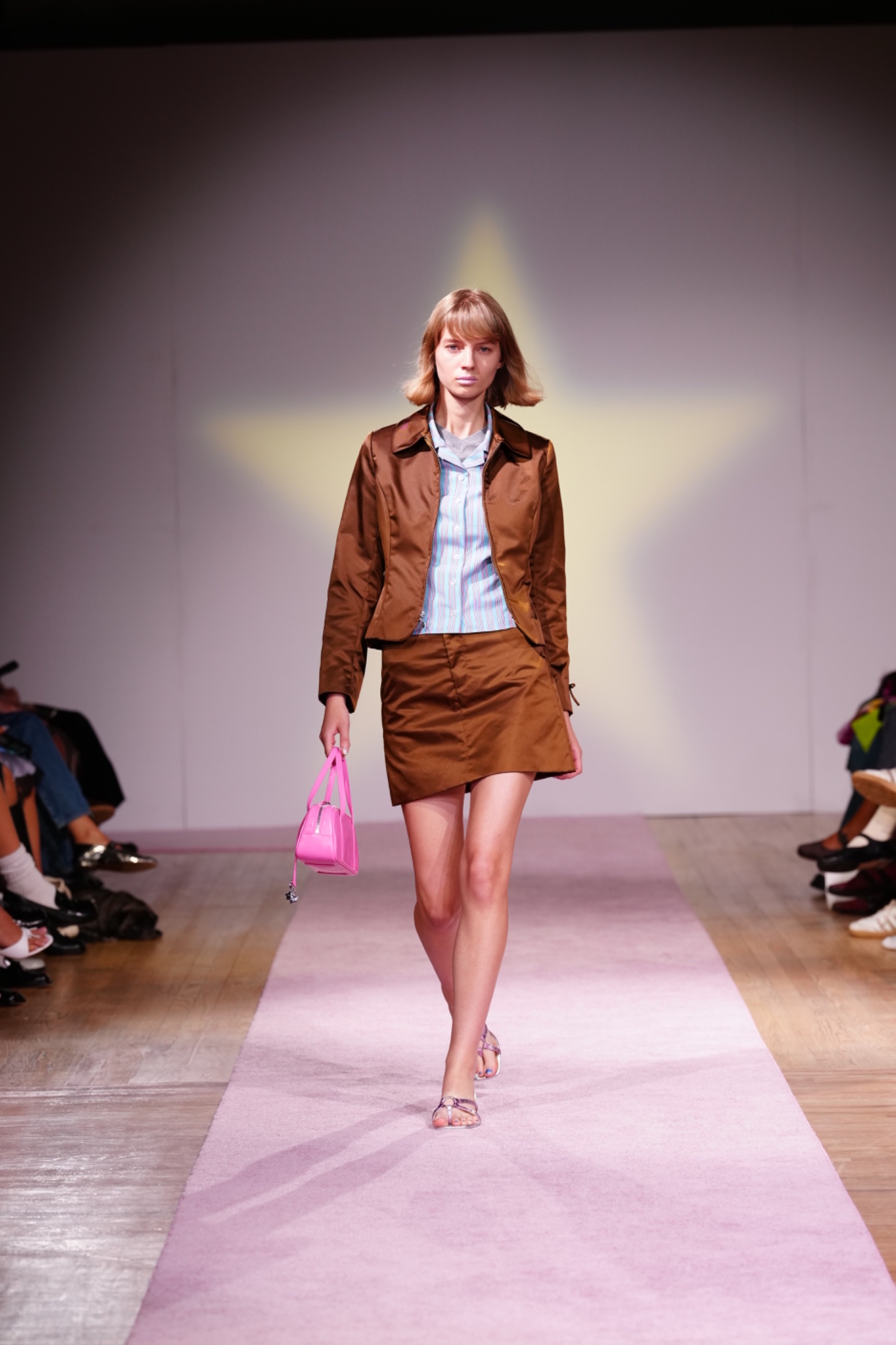 A model walking the runway wearing a blue shirt with a brown blazer and brown shorts.