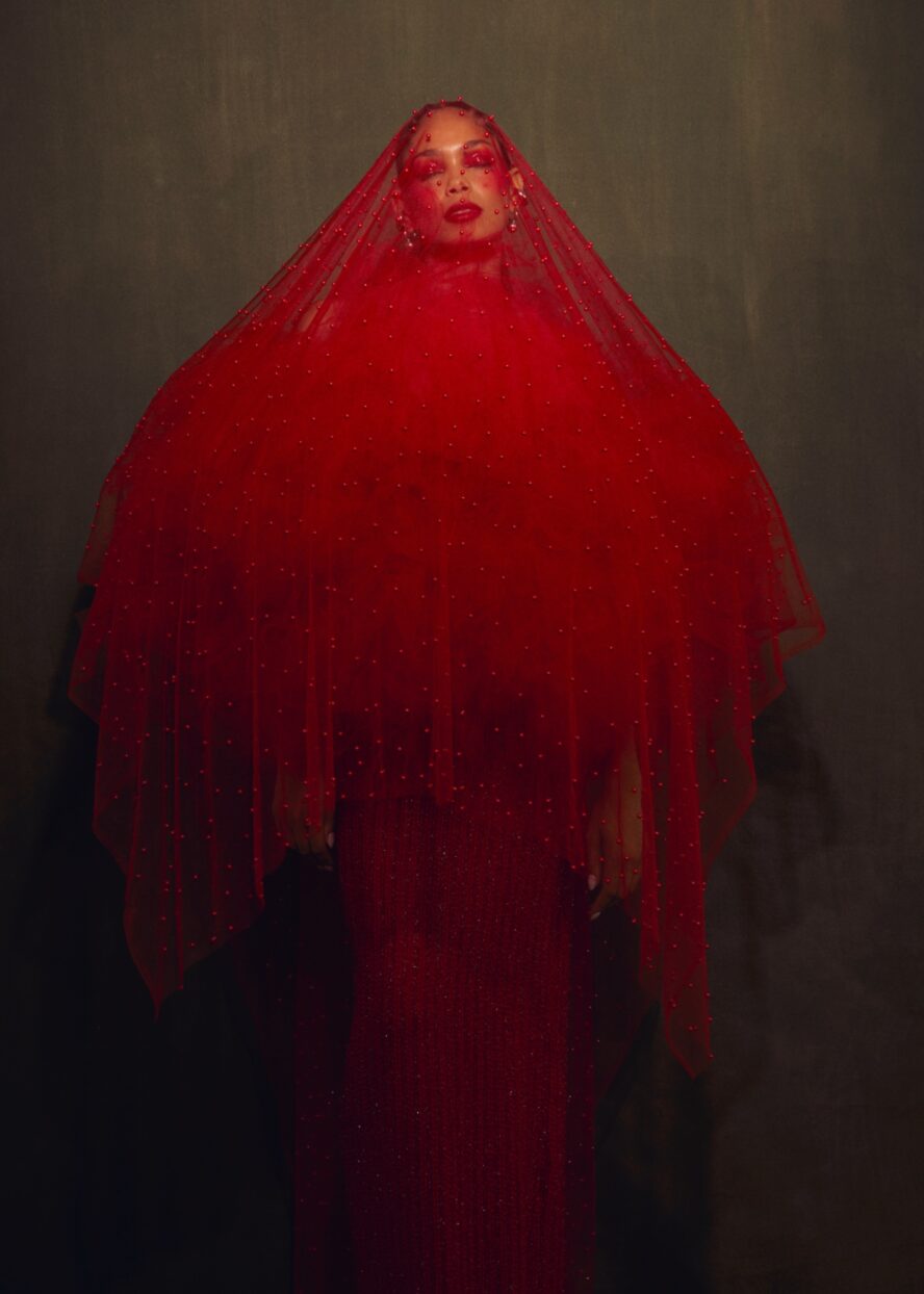 A model wearing a long red dress with red veil.