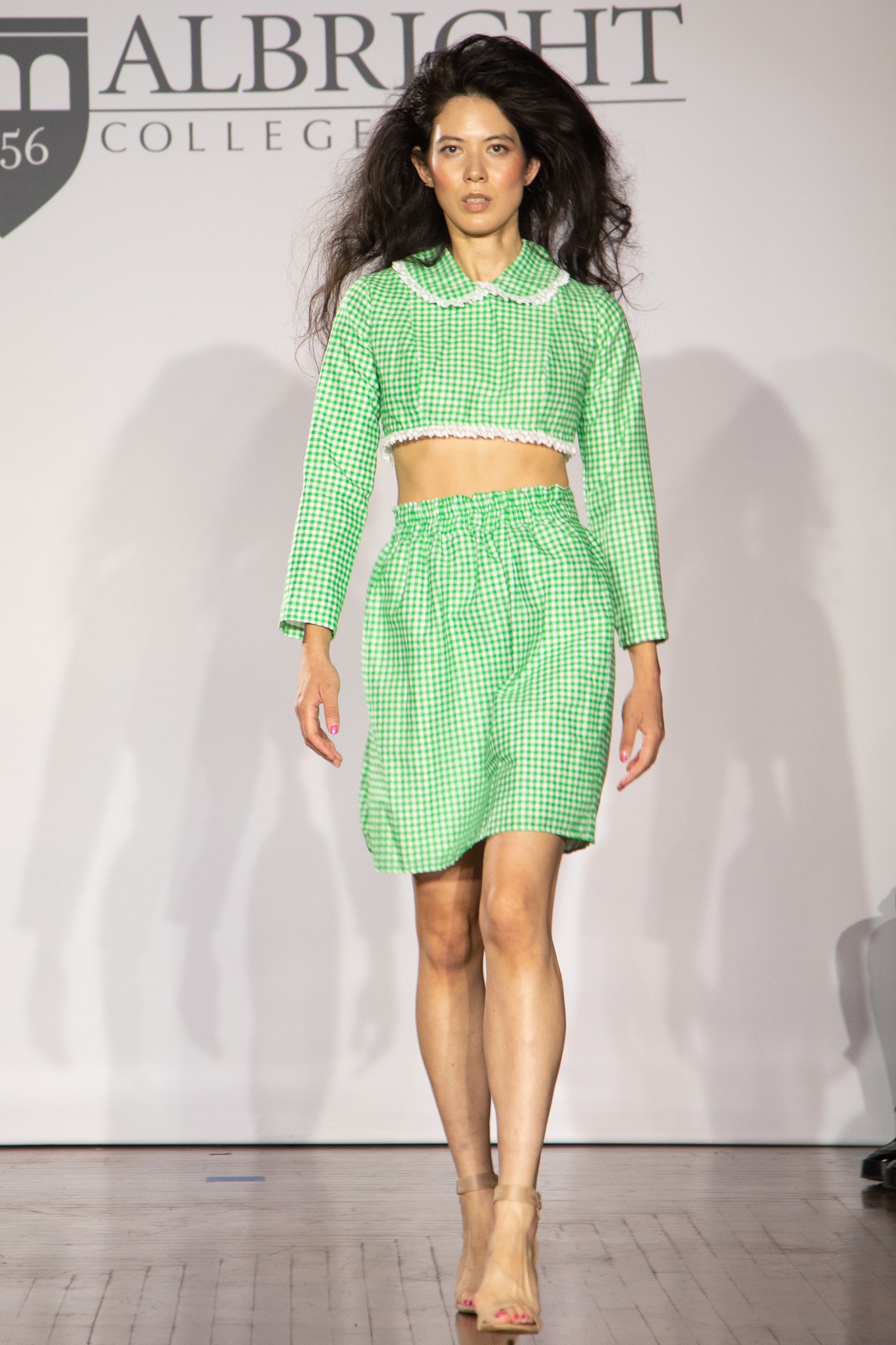 A model walking the runway wearing a green long-sleeved top and skirt.